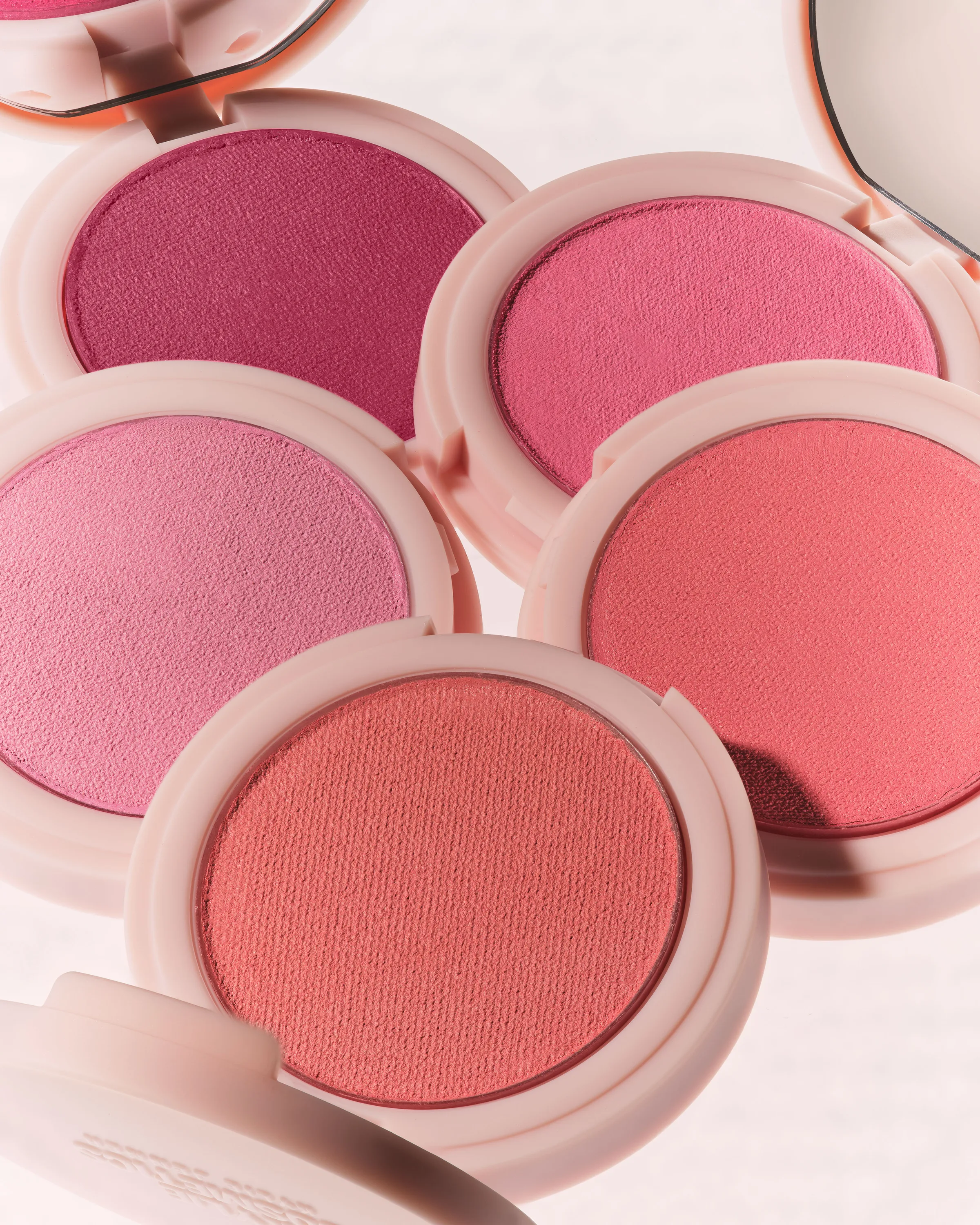 Open powder blush compacts in pink, berry and coral shades arranged in a cluster with pale pink cases, for Kylie Cosmetics.
