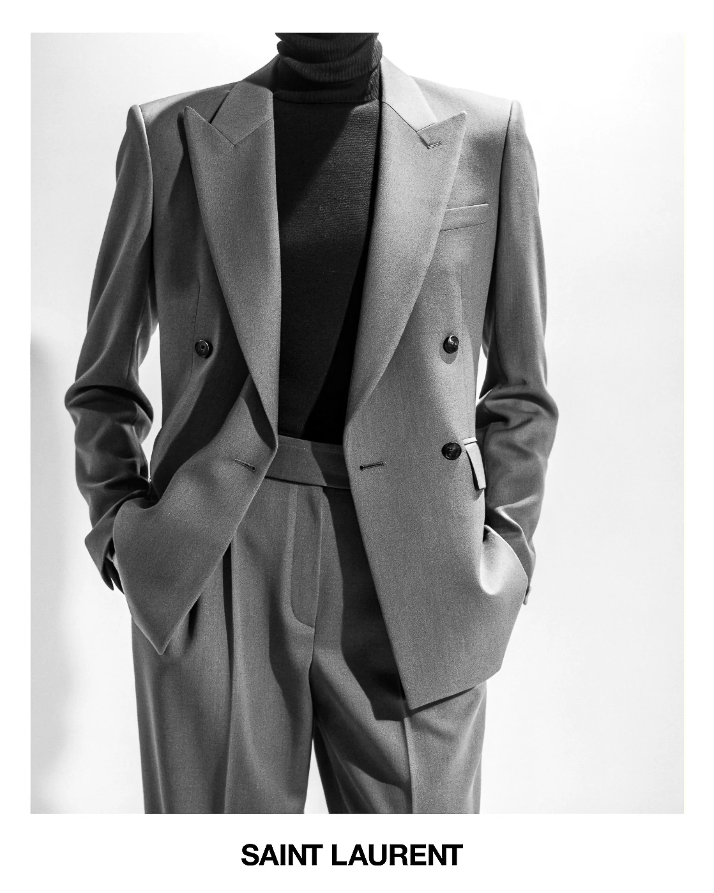 AI image of a model in a grey double-breasted suit and black turtleneck, hands in pockets, in black and white. Saint Laurent AI Concept.