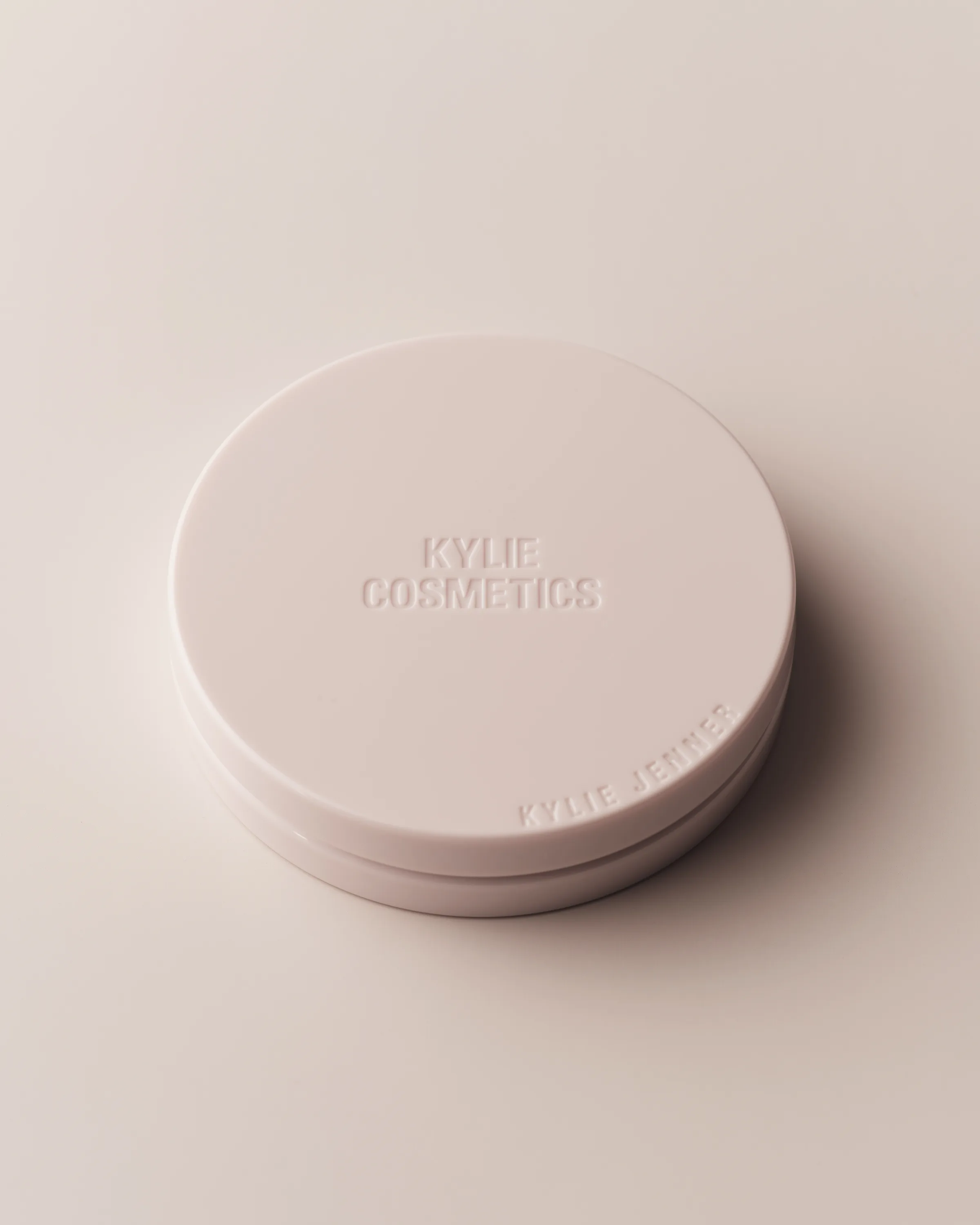 Closed pale pink compact with embossed Kylie Cosmetics lettering on a soft blush background, for Kylie Cosmetics.