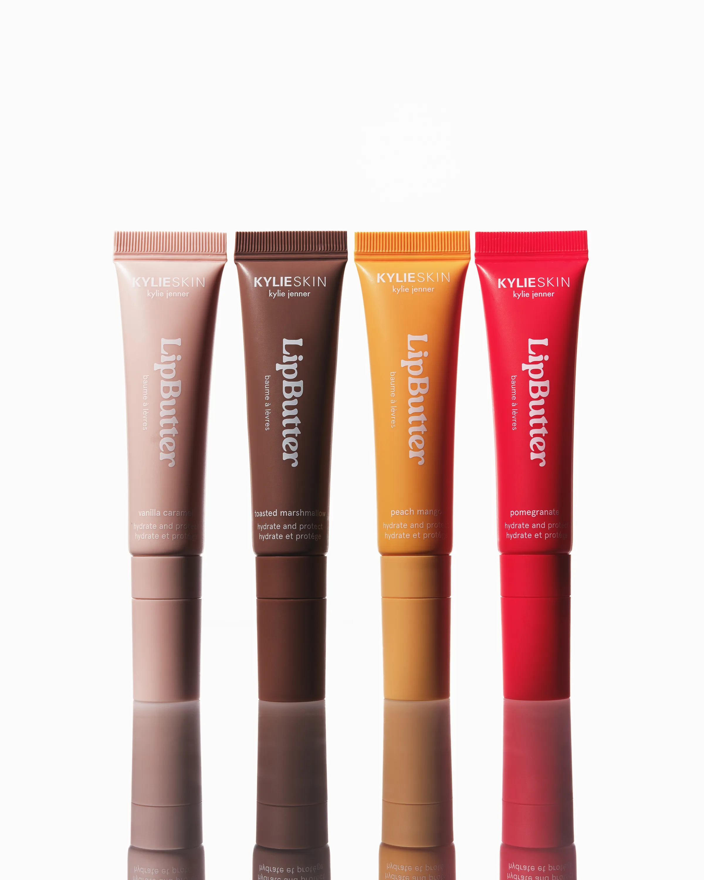 Four Lip Butter tubes in nude, brown, orange and red standing on a reflective white surface, for Kylie Skin.