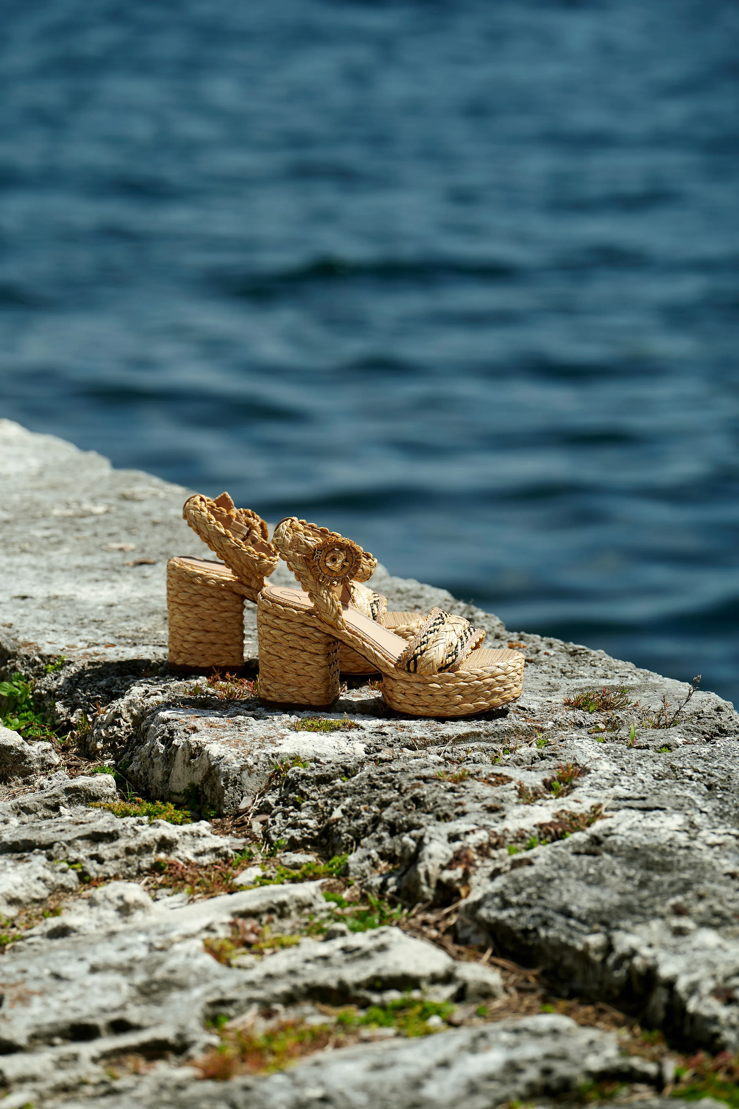 Woven raffia platform sandals resting on a rocky ledge above blue water, for Sam Edelman.