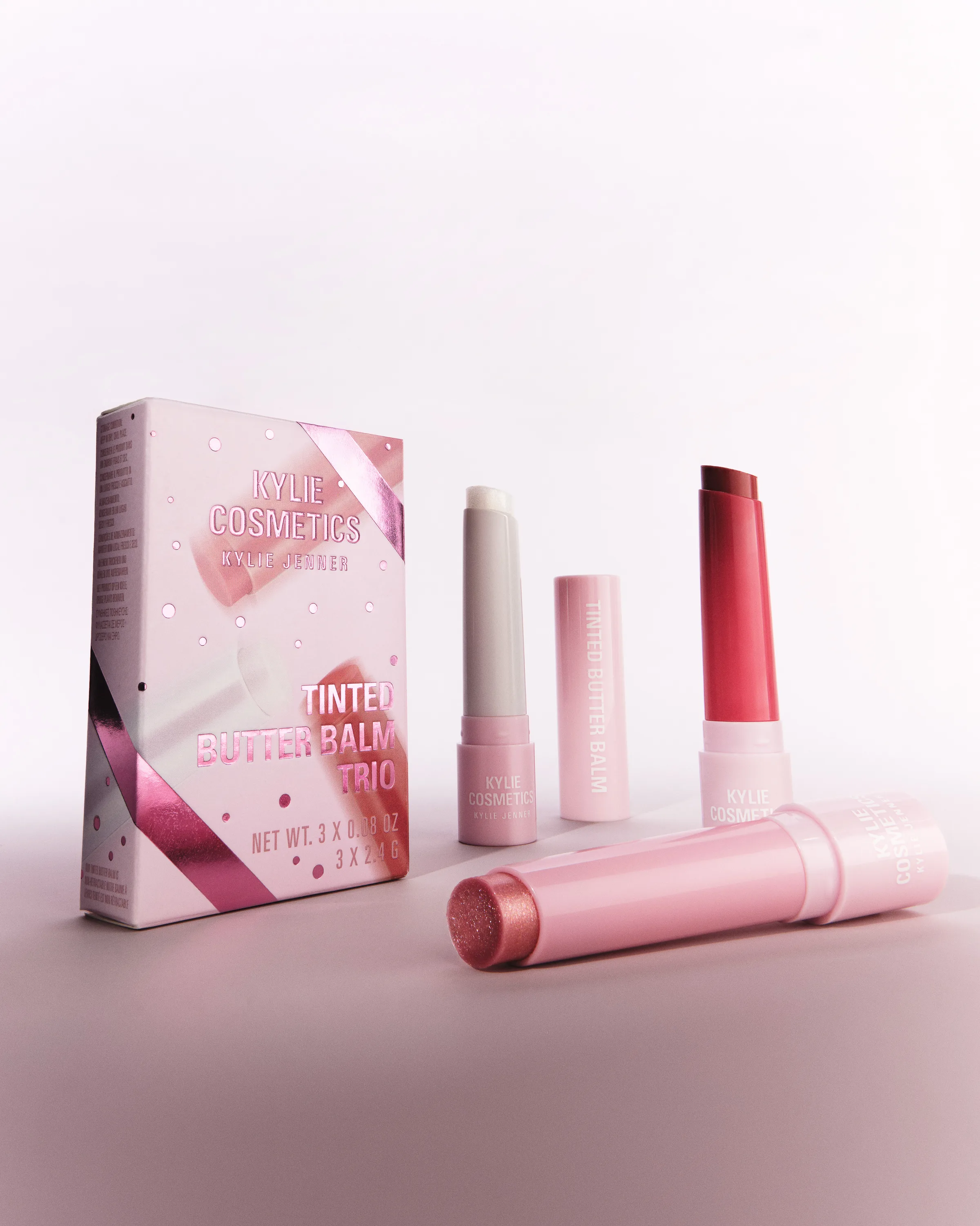 Tinted Butter Balm Trio box with three pink lip balms, one lying open in front, on a soft pink backdrop, for Kylie Cosmetics.