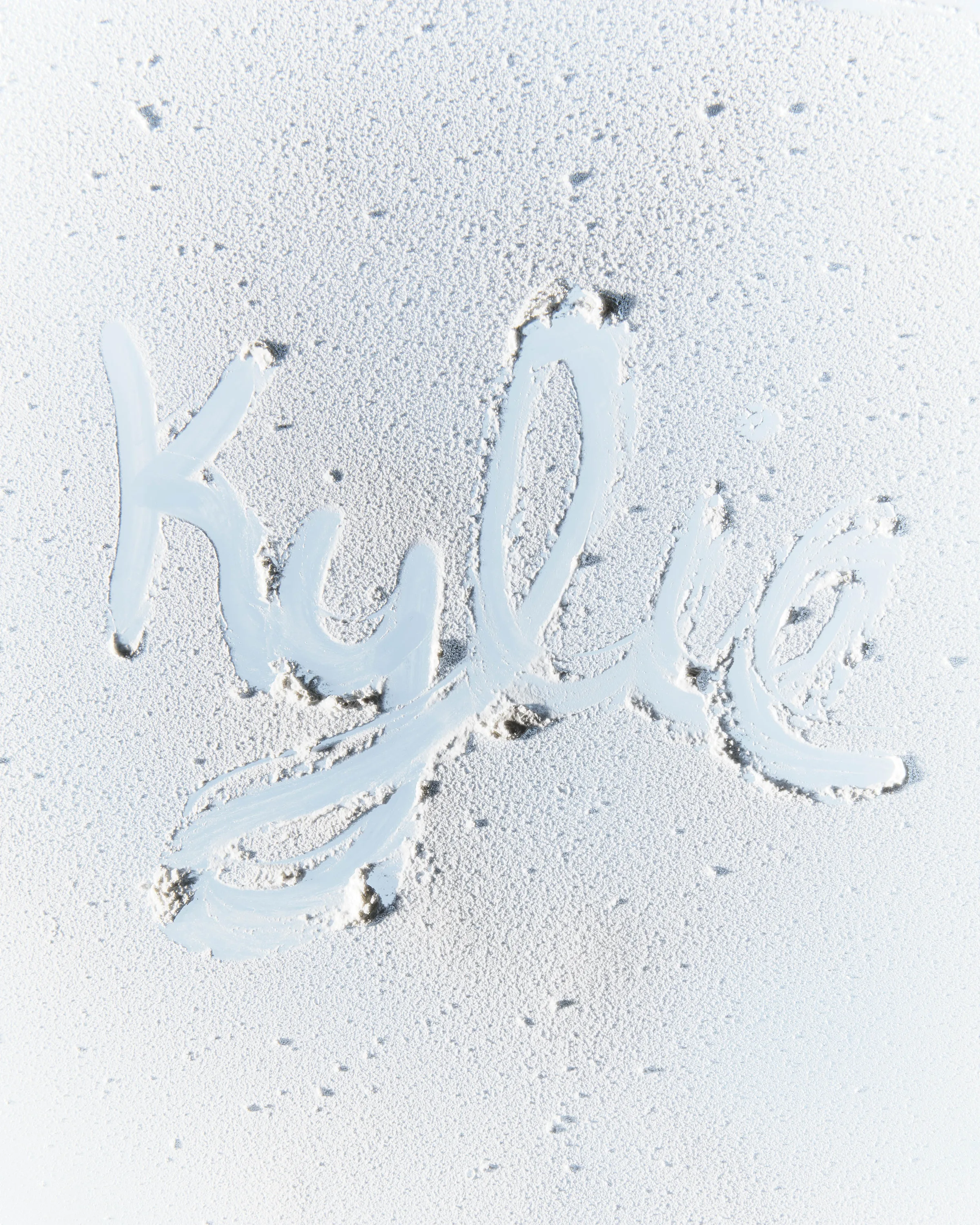 Kylie signature script traced through frost on a pale icy glass surface for a holiday campaign, for Kylie Cosmetics.
