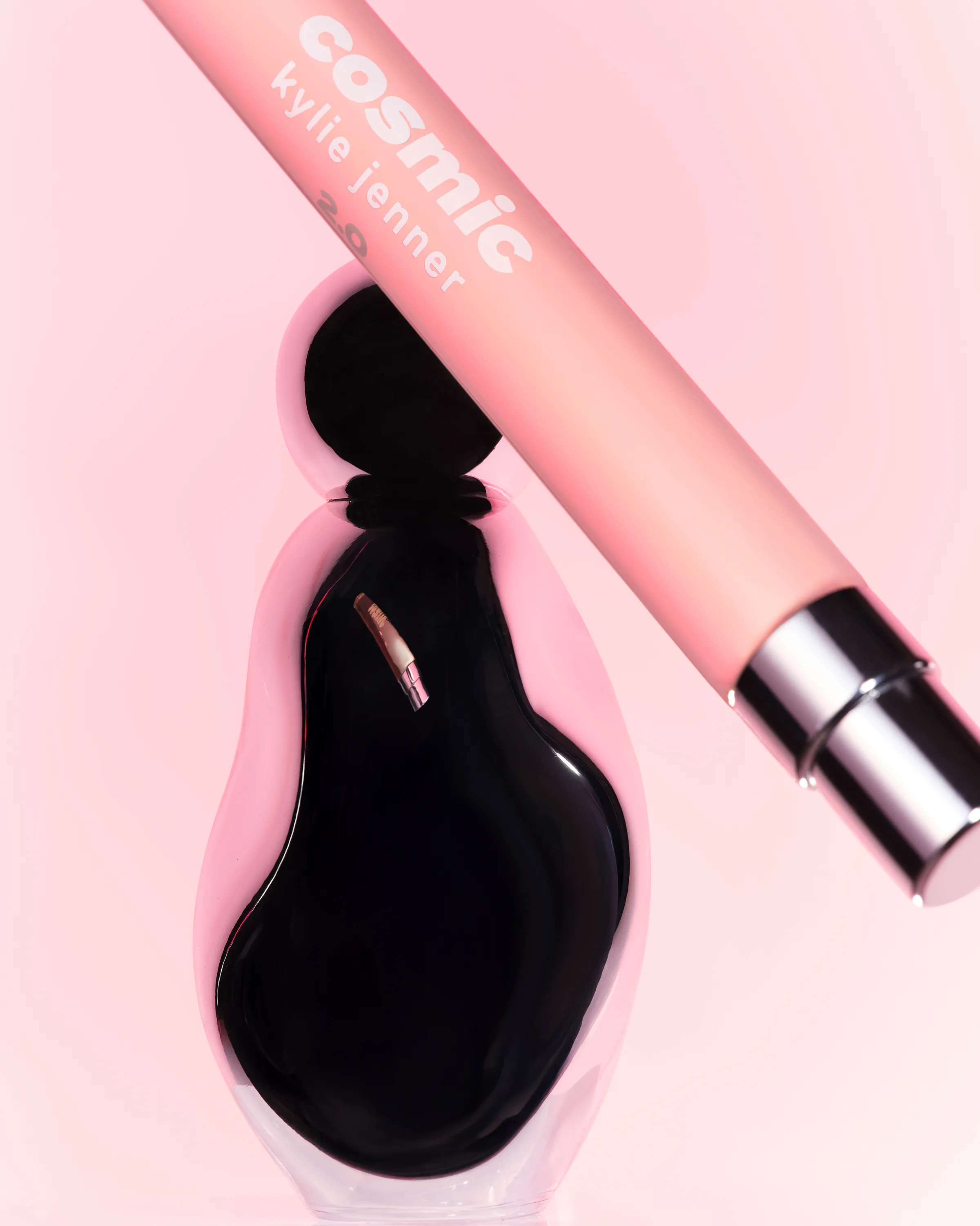 Cosmic eau de parfum bottle with a pink 10ml pen spray resting across it on a soft pink backdrop, for Kylie Cosmetics.