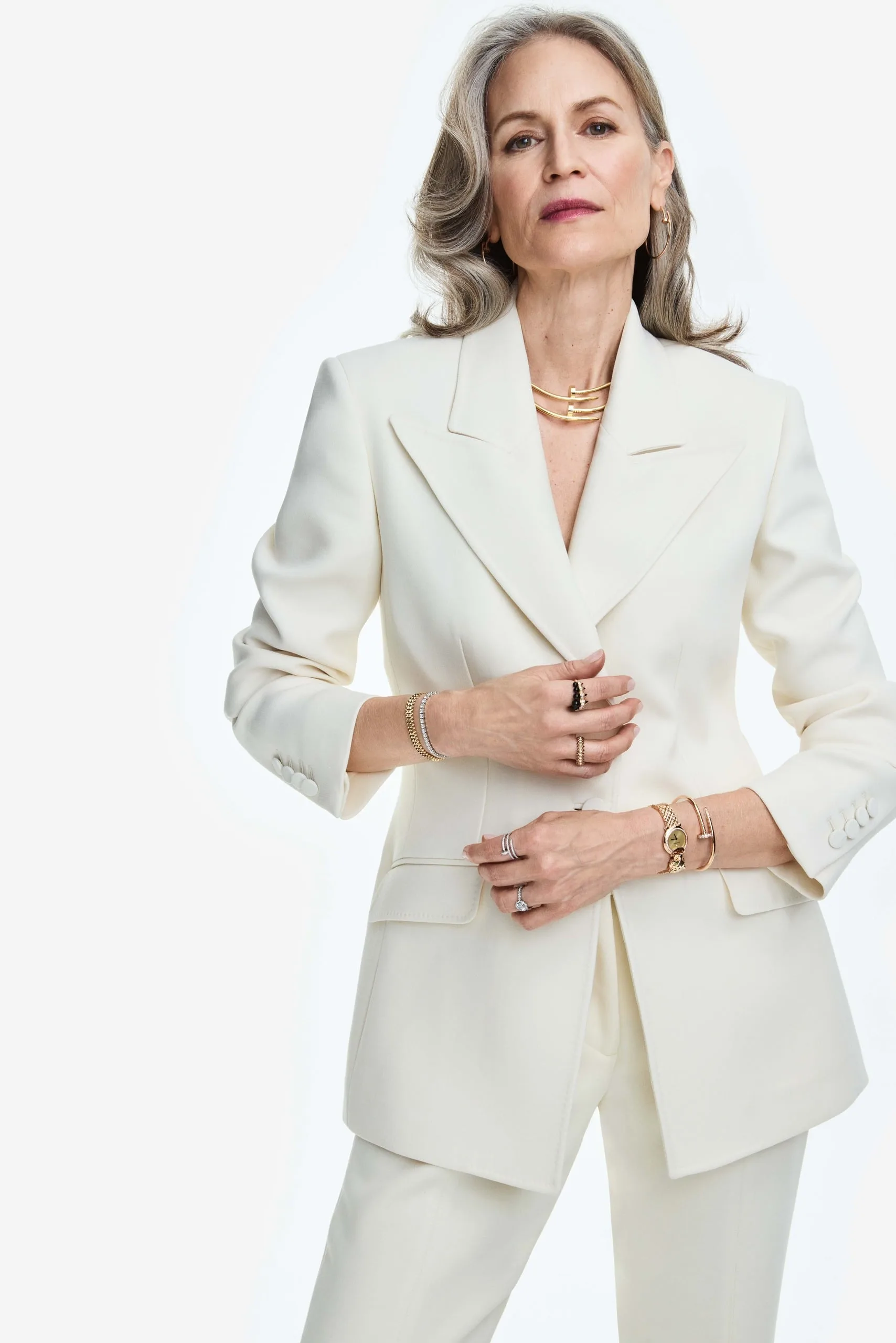 Silver-haired model in an ivory double-breasted suit wearing stacked gold necklaces, bracelets and rings, for Cartier.