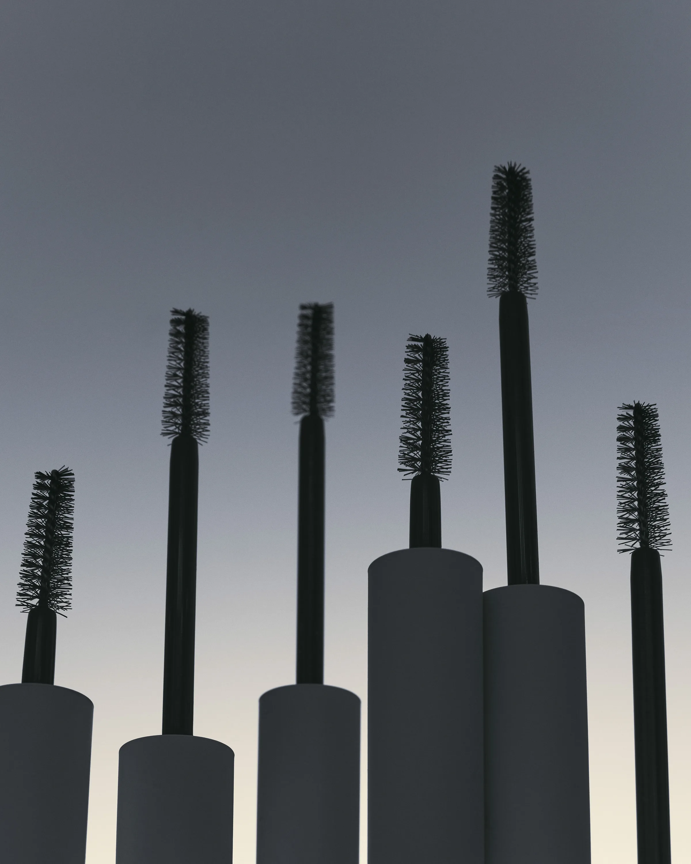Six mascara wands rising from white cylindrical pedestals, silhouetted against a grey dusk gradient, for Kylie Cosmetics.