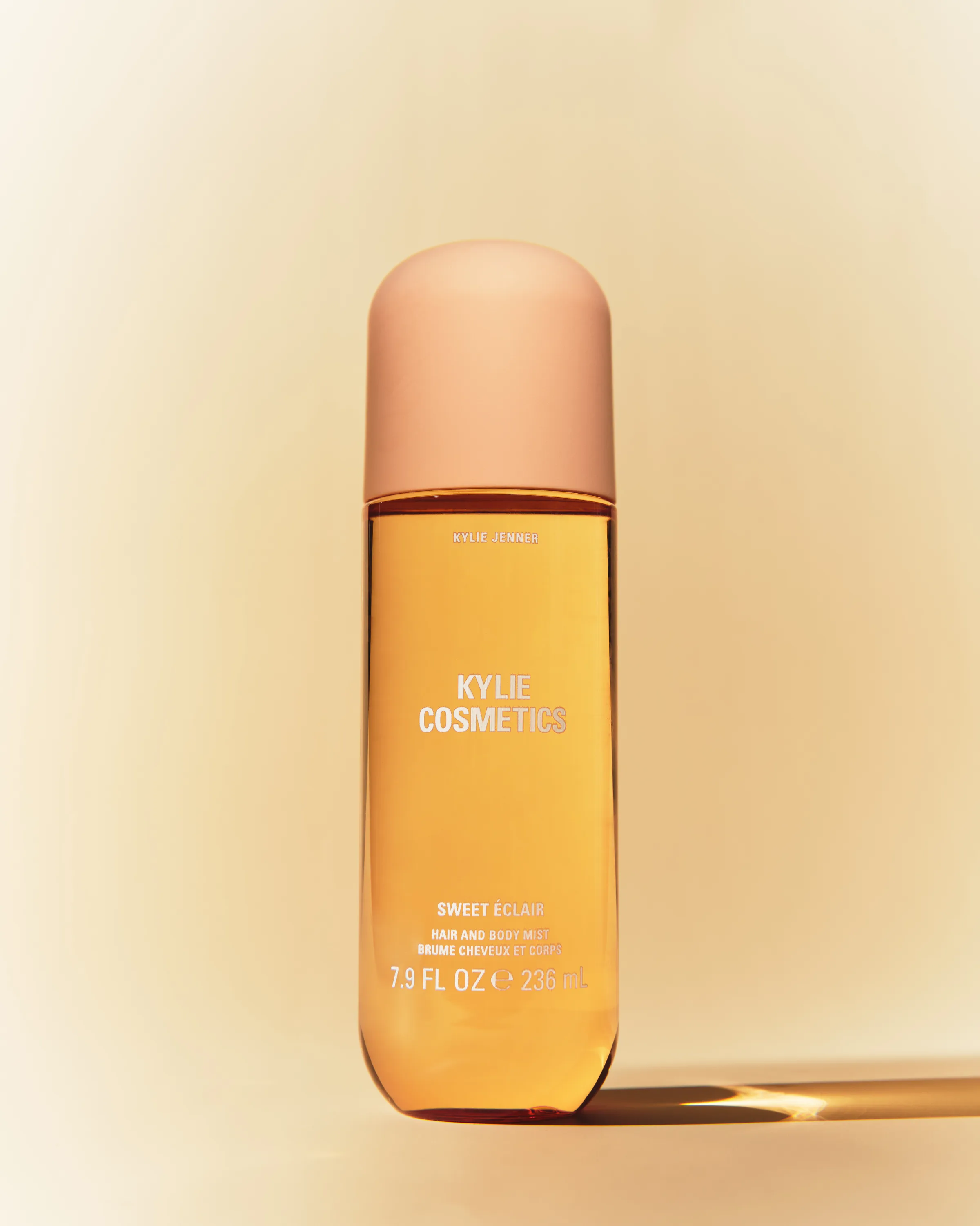 Sweet Eclair hair and body mist bottle with peach cap on a warm cream backdrop with hard sunlight, for Kylie Cosmetics.