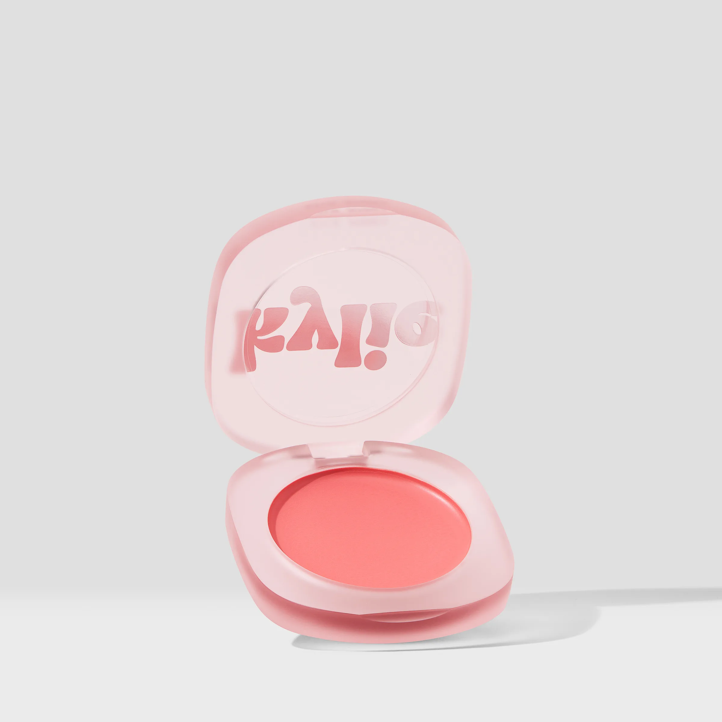 Open pink frosted compact of coral pressed blush with kylie logo on the lid, on a light grey backdrop, for Kylie Cosmetics.