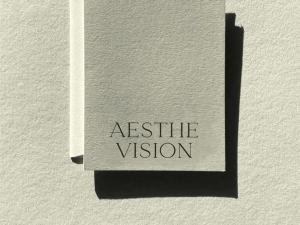 Pale grey textured card printed with the Aesthe Vision wordmark, casting a hard shadow on paper, for Aesthevision.