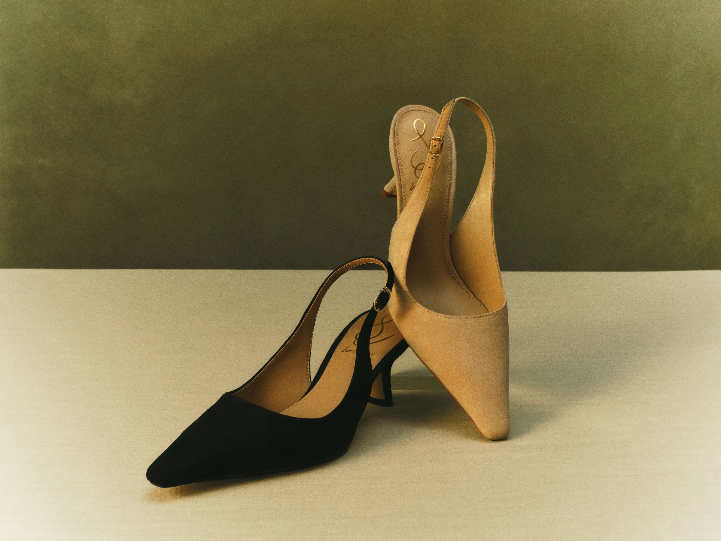 Black and cappuccino suede slingback kitten heels on a linen table against an olive backdrop, for Sam Edelman.
