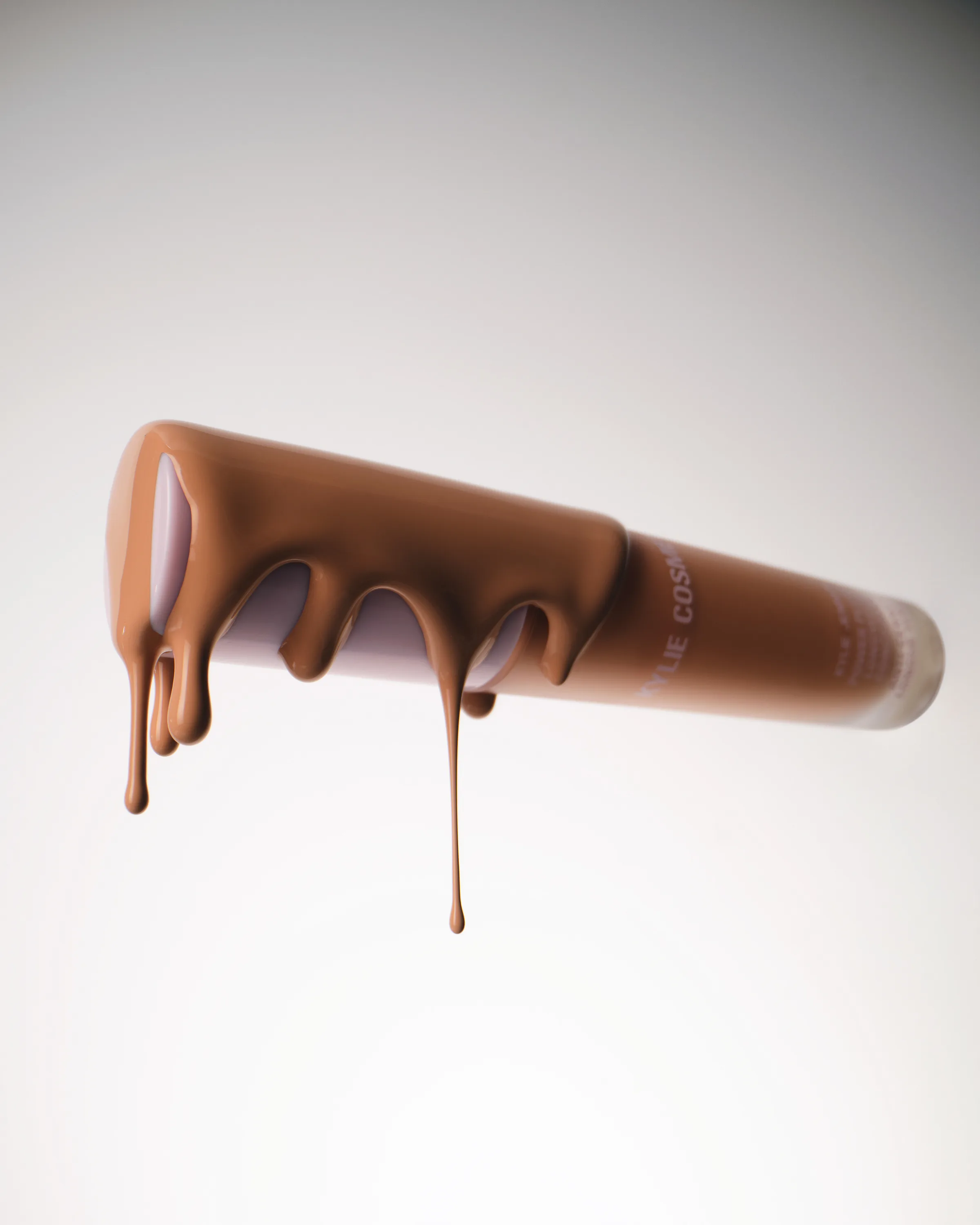 Floating foundation tube coated in dripping tan liquid against a soft white backdrop, for Kylie Cosmetics.