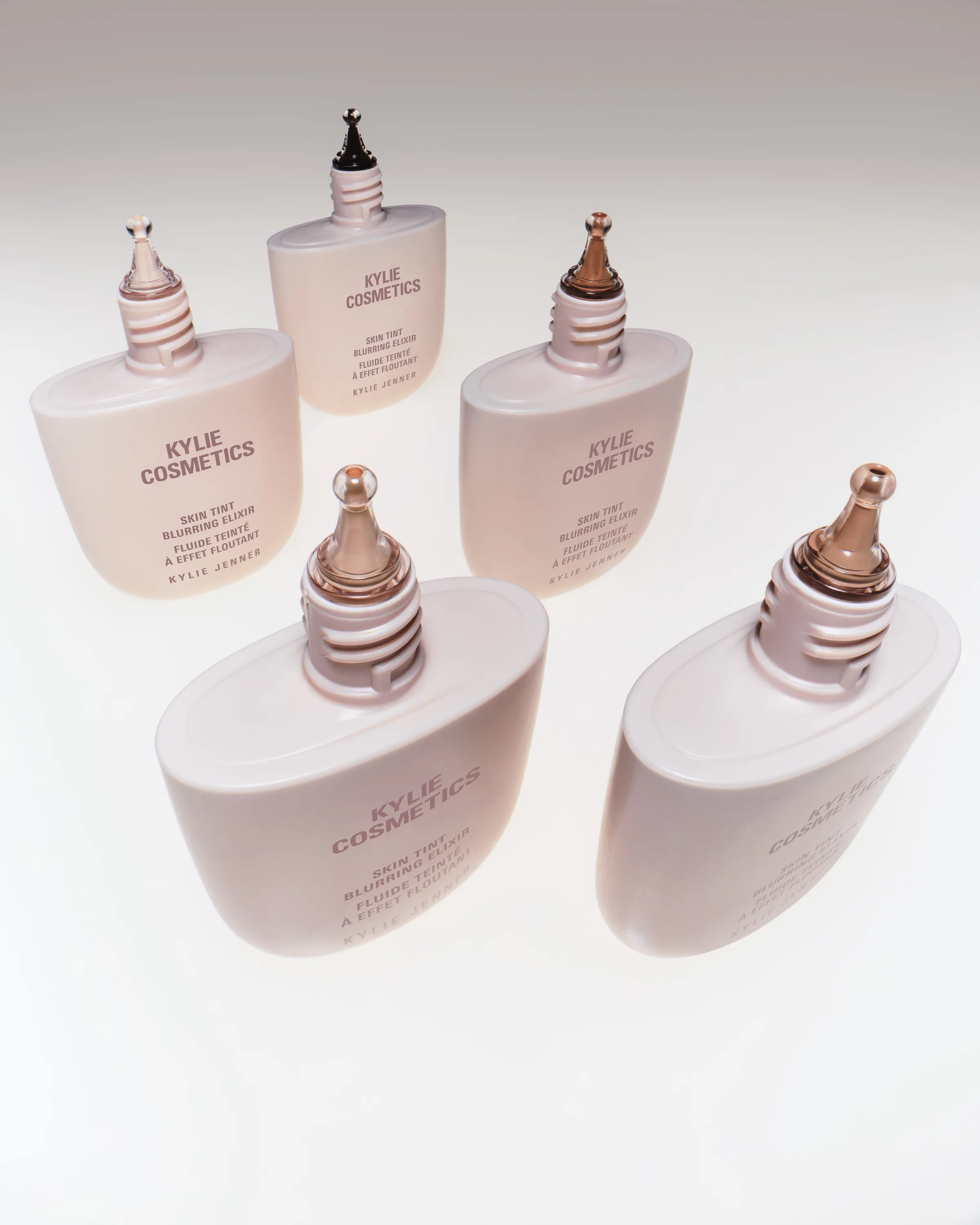 Five pale pink Skin Tint Blurring Elixir bottles with metallic droppers on a white surface, for Kylie Cosmetics.