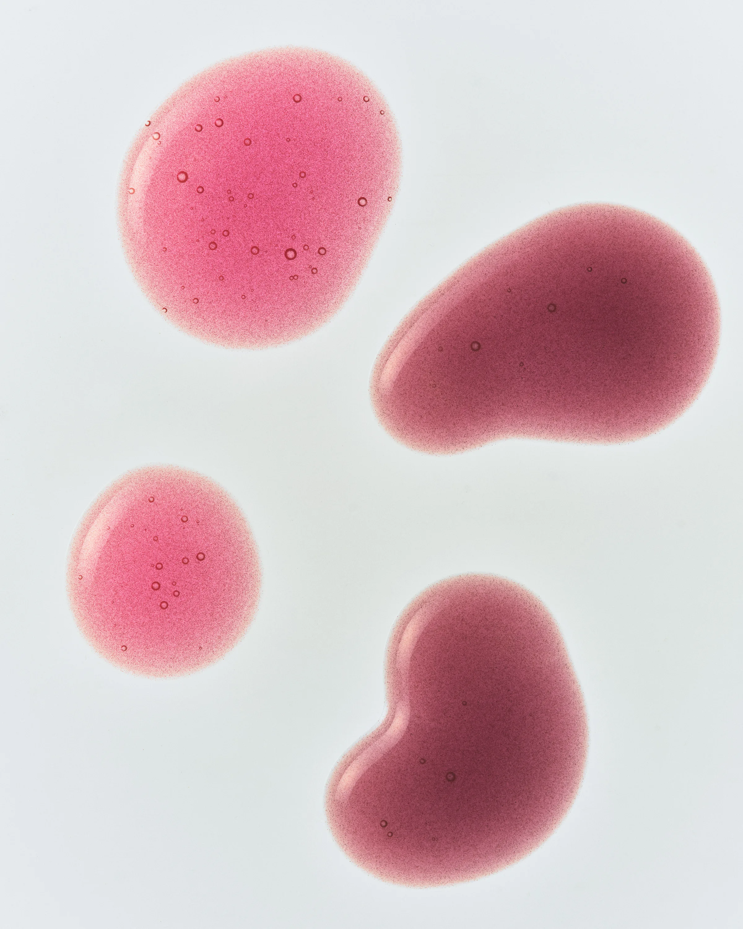 Four glossy swatches of pink and berry tinted gloss with tiny bubbles on a white surface, for Kylie Cosmetics.