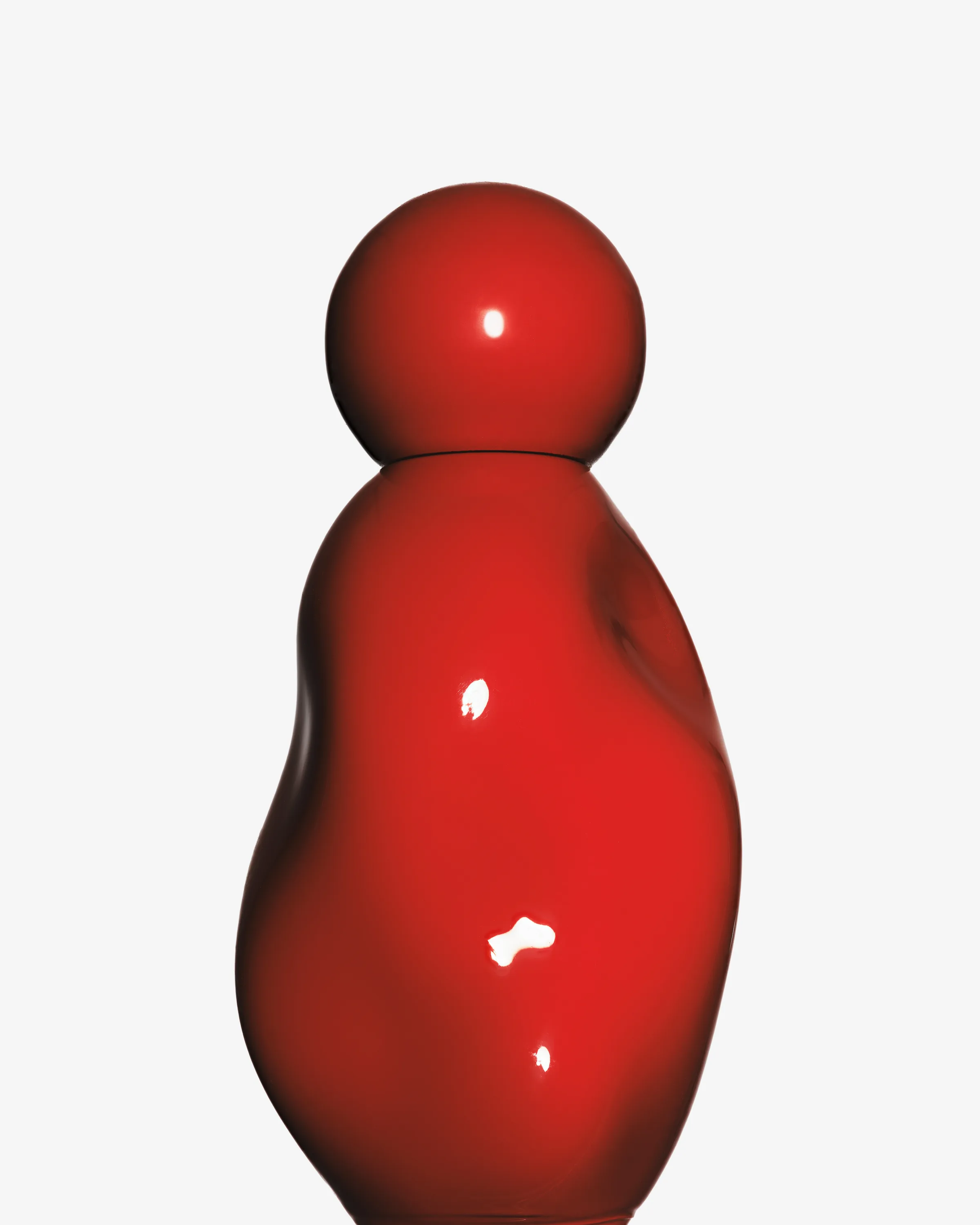 Glossy red sculpted perfume bottle with round cap on a light grey background, for Kylie Cosmetics.