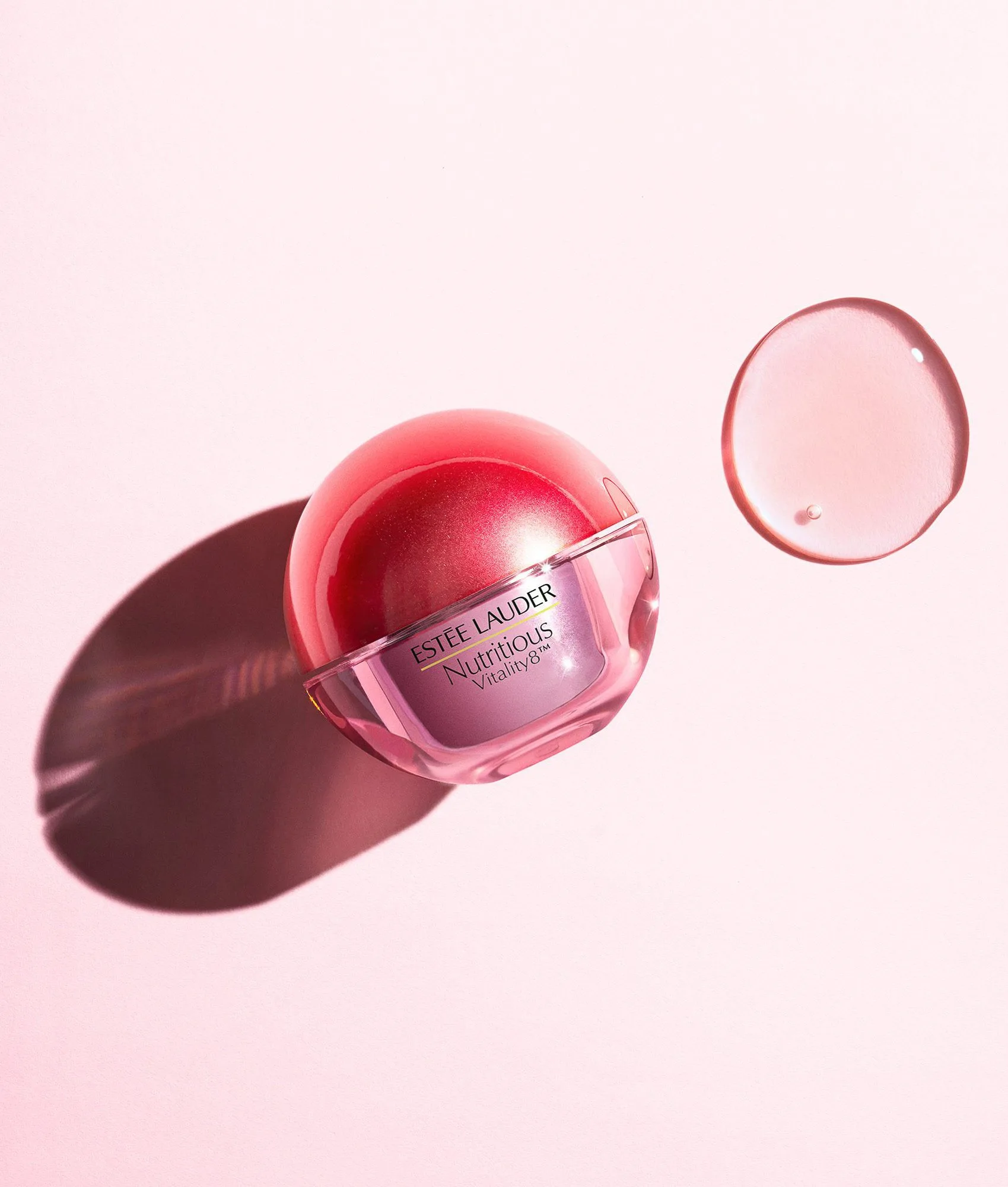 Red Nutritious Vitality8 jar beside a clear gel swatch on pink, with hard shadow, for Estée Lauder.