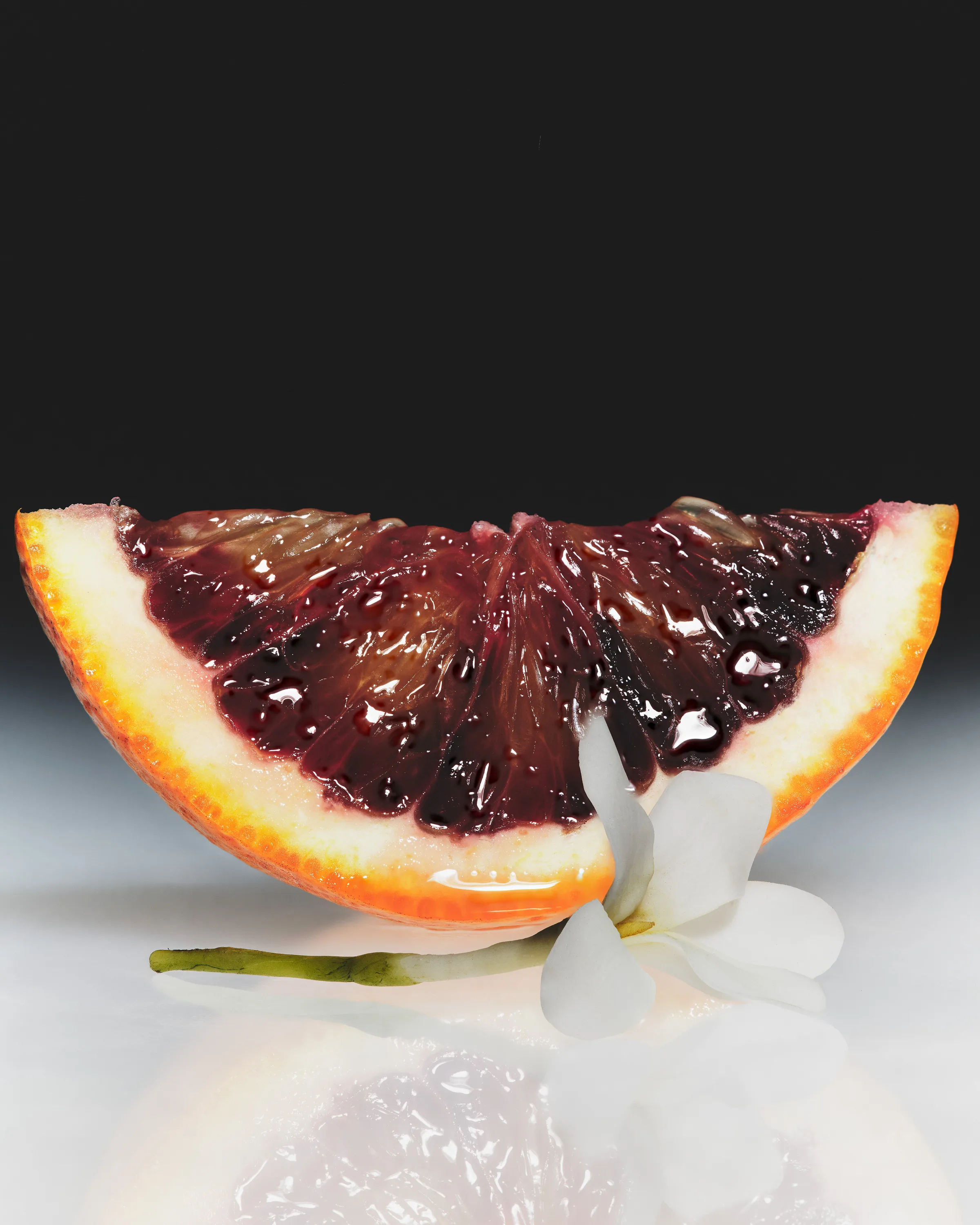 Still life of a glossy blood orange wedge with a white star jasmine flower on a reflective surface, for Kylie Cosmetics.