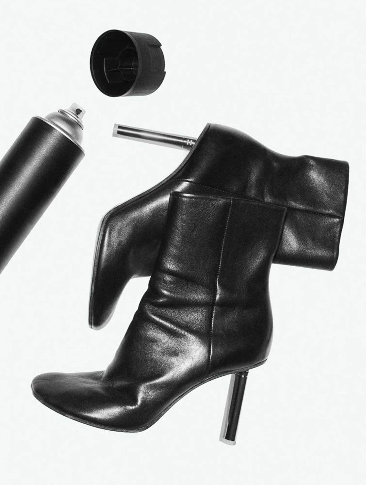 Black leather ankle boots with chrome heels beside an open black spray can on white, for Interview Magazine.