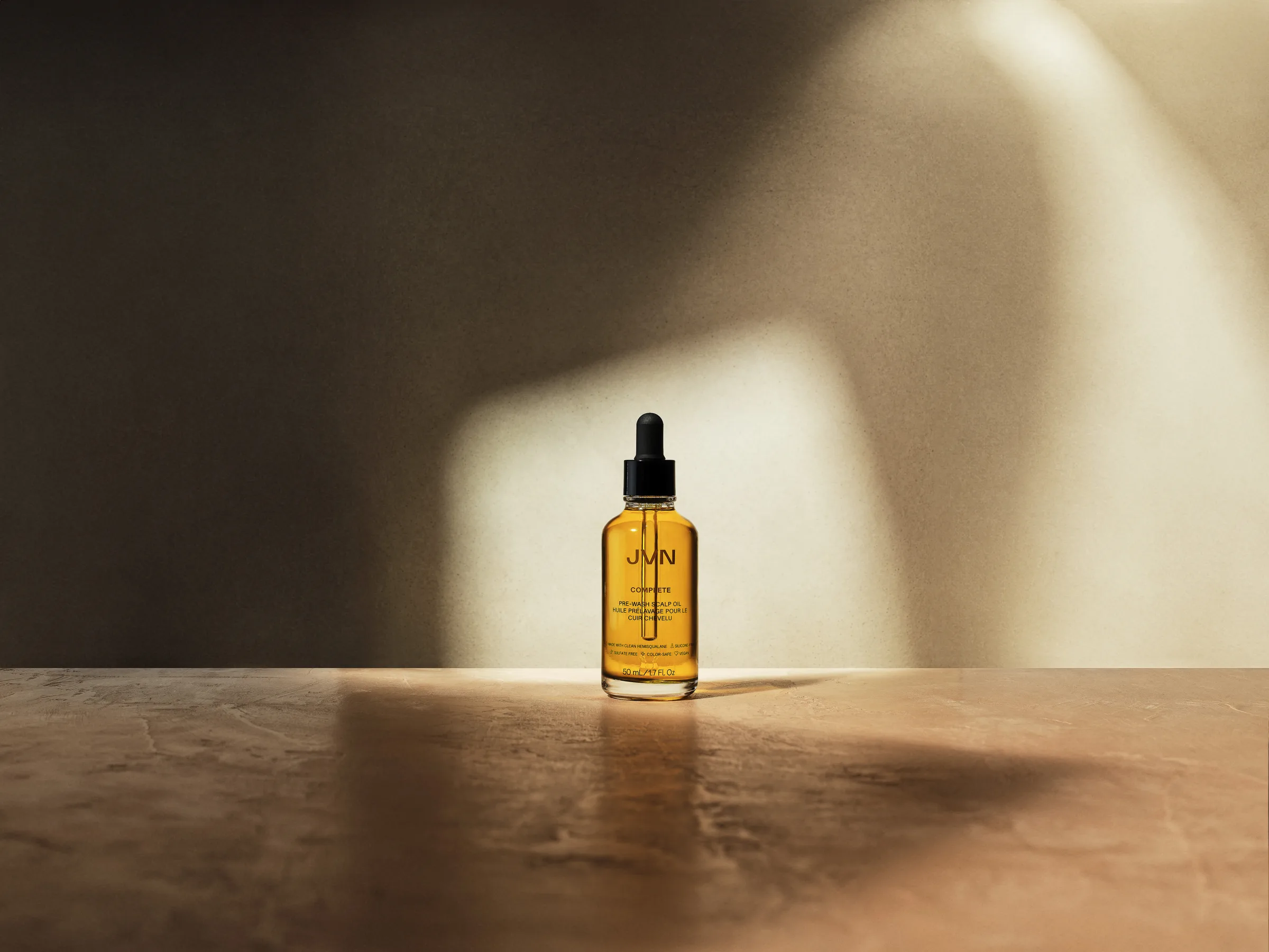 Amber JVN Complete scalp oil dropper bottle on a stone surface in warm angled sunlight and shadow, for JVN.