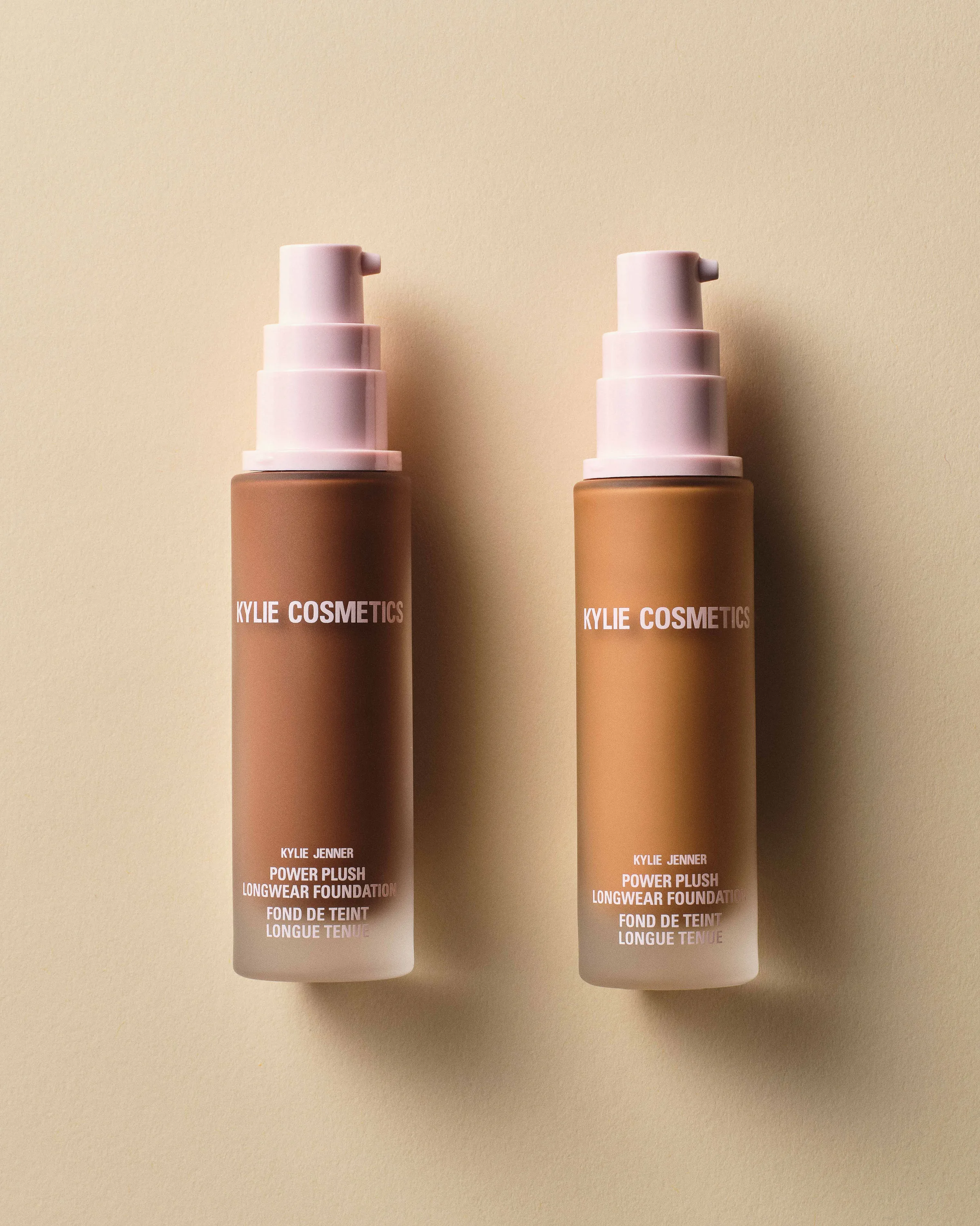 Two Power Plush Longwear Foundation bottles in deep and tan shades with pink pumps on a beige backdrop, for Kylie Cosmetics.