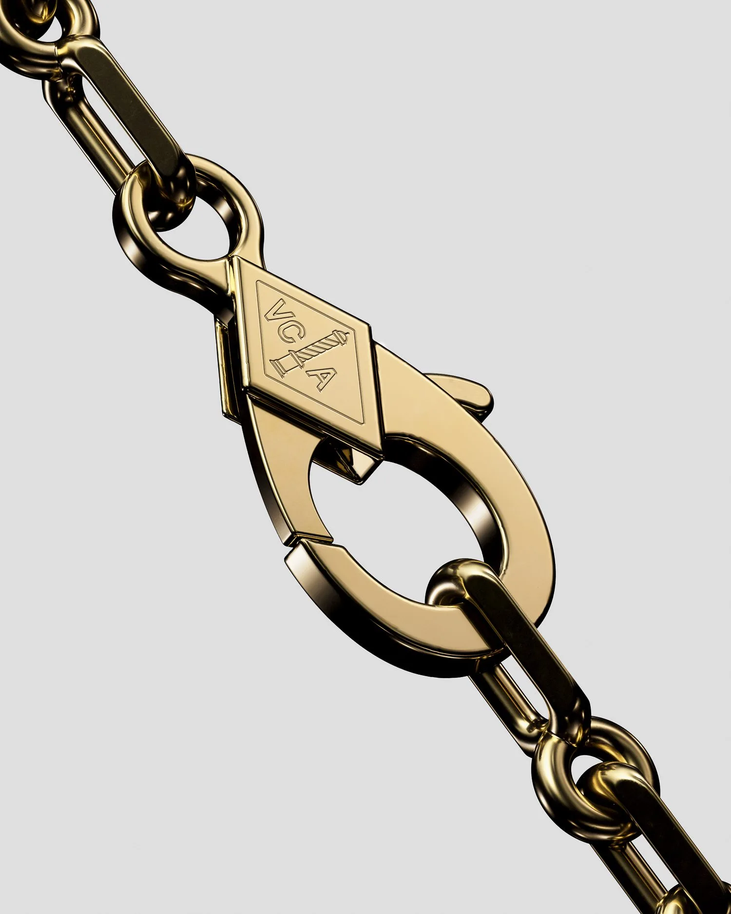 CGI render of a gold chain with a VCA-engraved lobster clasp on a pale grey background, for Van Cleef & Arpels.