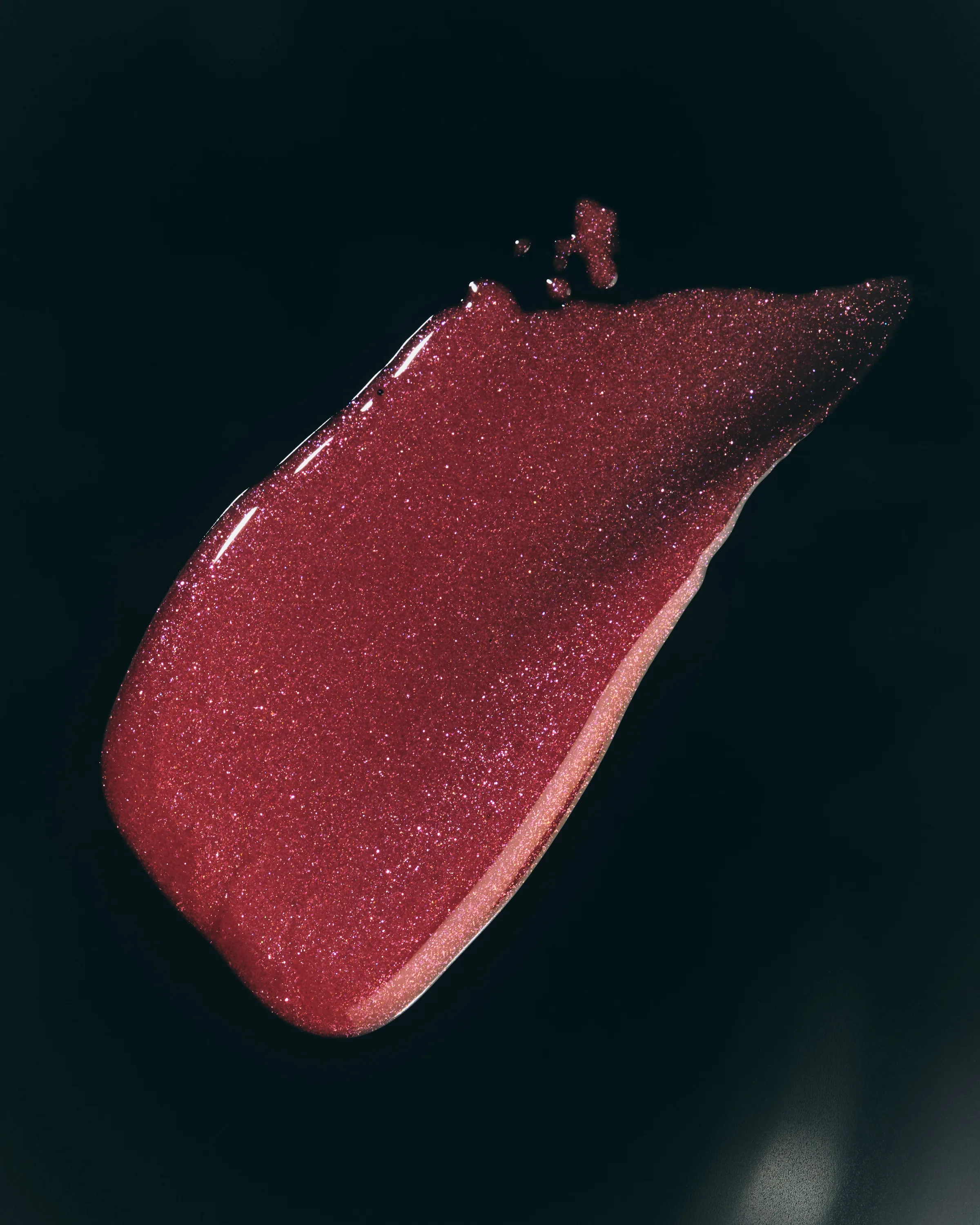 Swatch of shimmering berry-red lip glaze smeared across a black background, for Kylie Cosmetics.