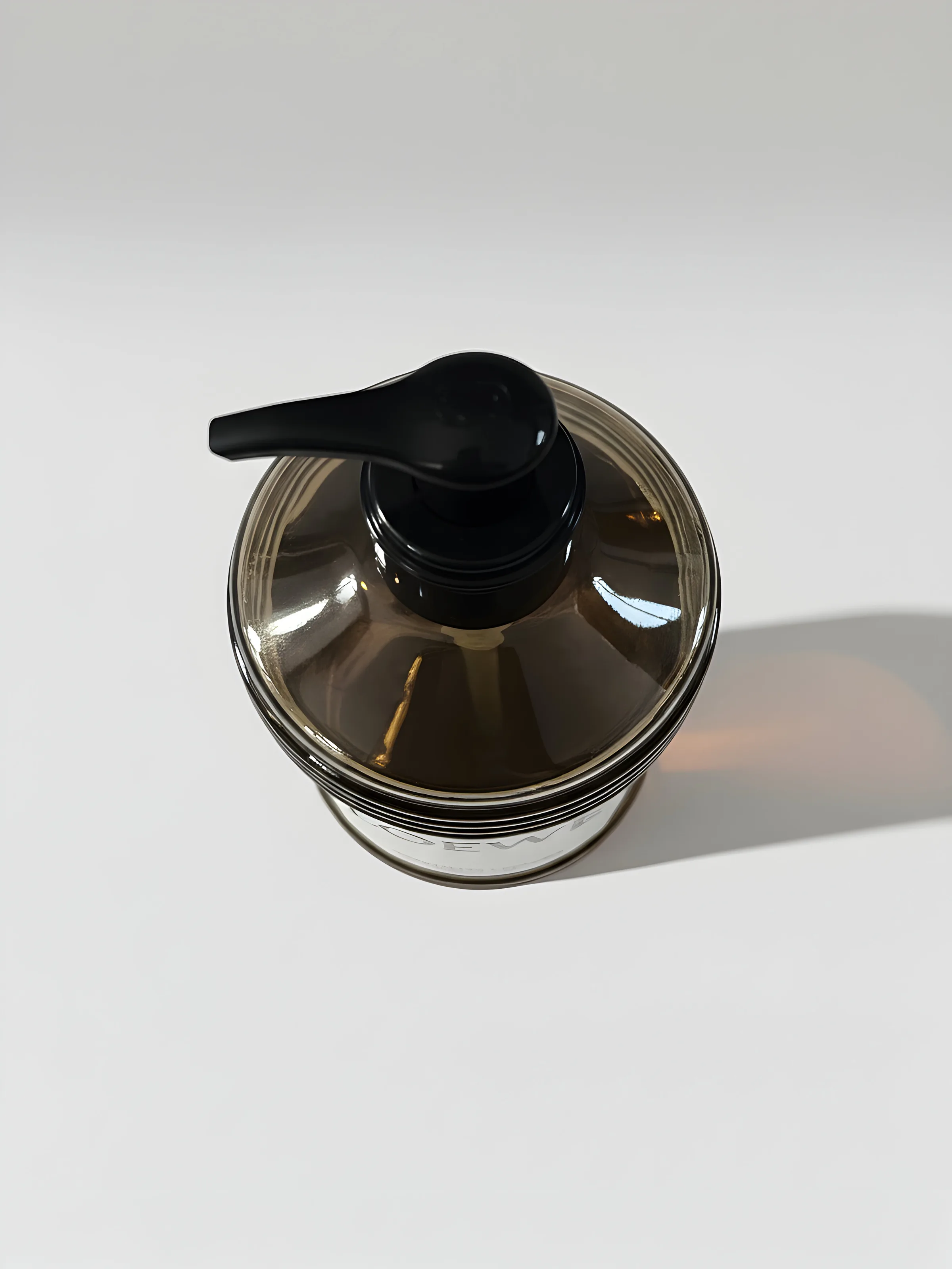 AI image of an amber glass pump bottle with a black dispenser, seen from above on a white surface. Loewe AI Concept.
