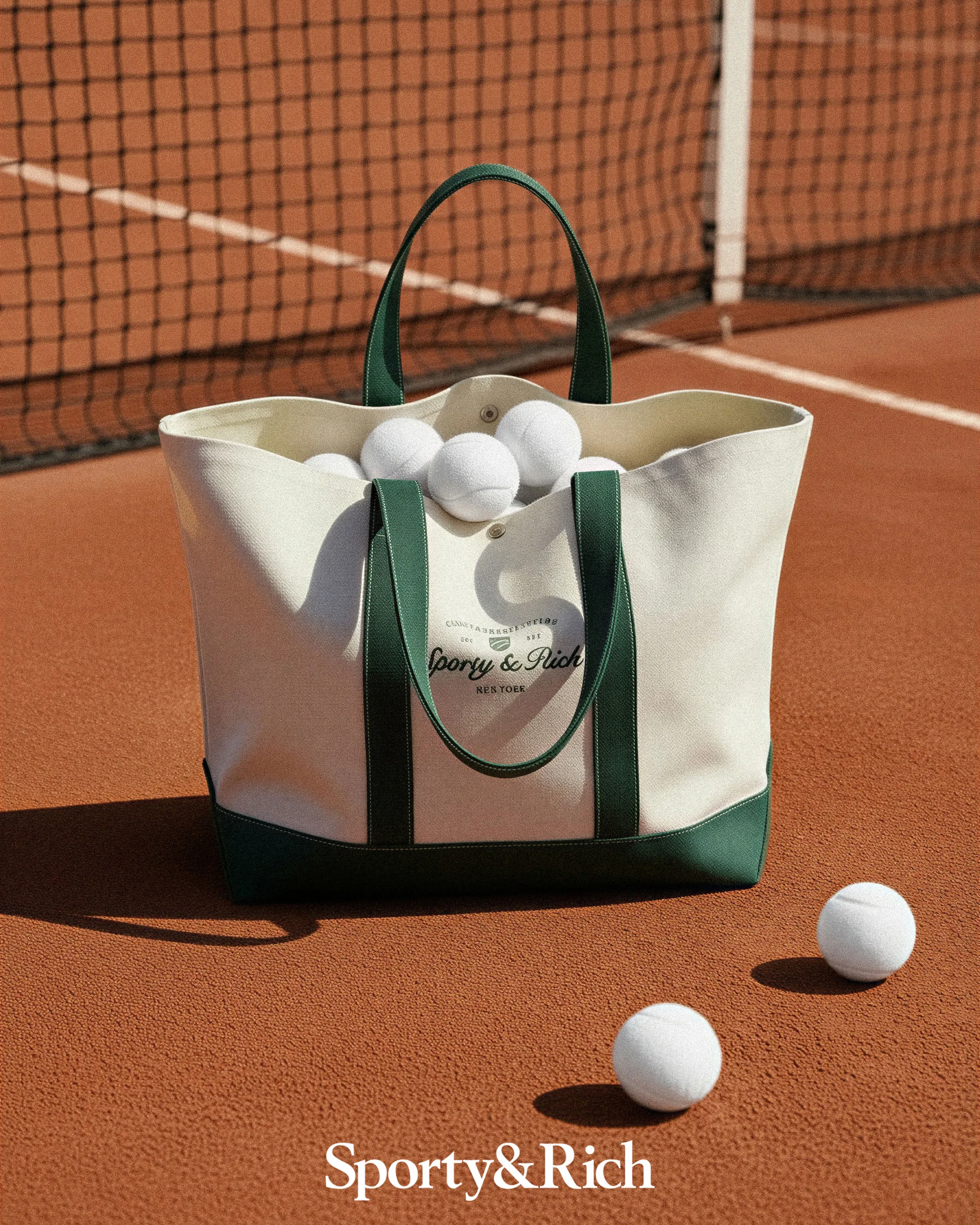 AI image of a cream canvas tote with green handles full of white tennis balls on a clay court. Sporty & Rich AI Concept.