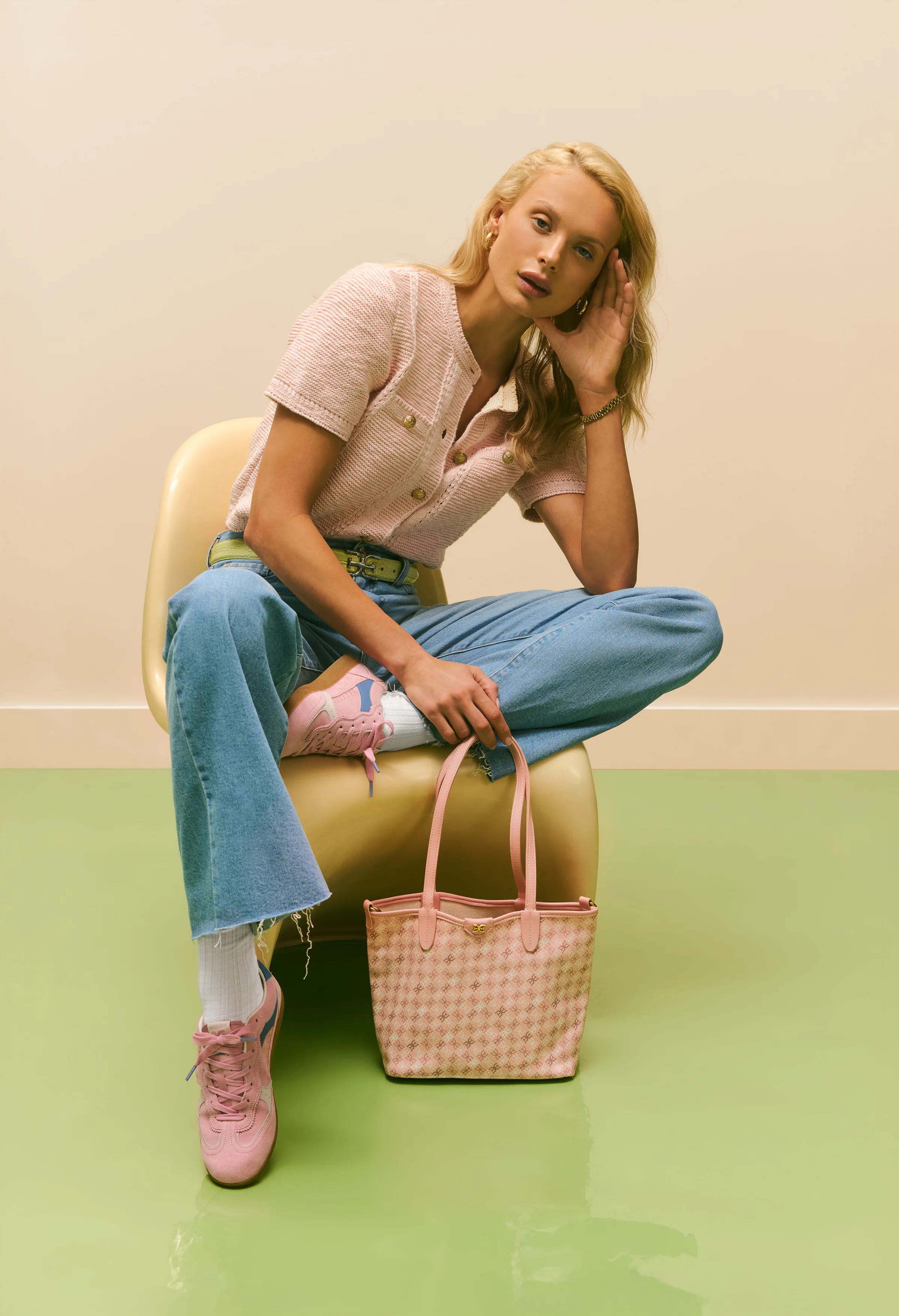 Model in pink tweed top and wide jeans sits on a cream chair with pink sneakers and a checked tote, for Sam Edelman.