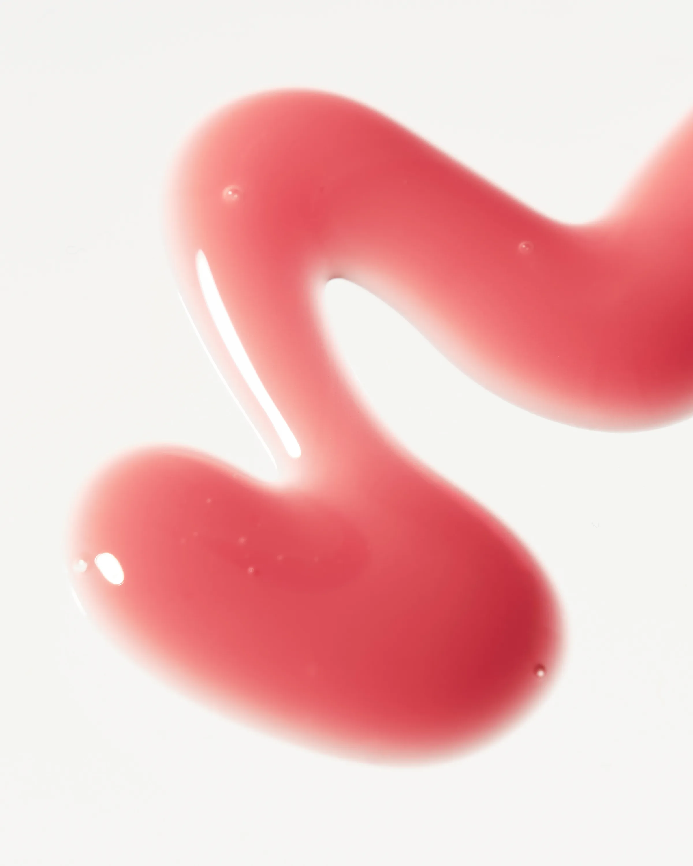 Glossy pink lip gloss swatch in a wavy S shape on a white background, for Kylie Cosmetics.