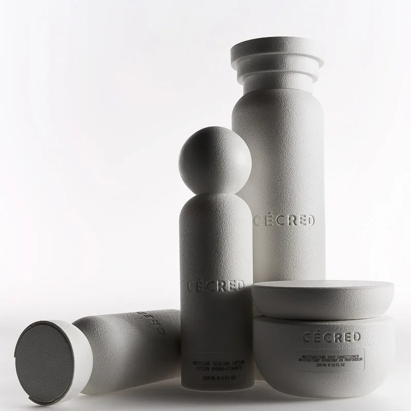 Textured white haircare bottles and conditioner jar grouped on a pale grey backdrop, for Cécred.