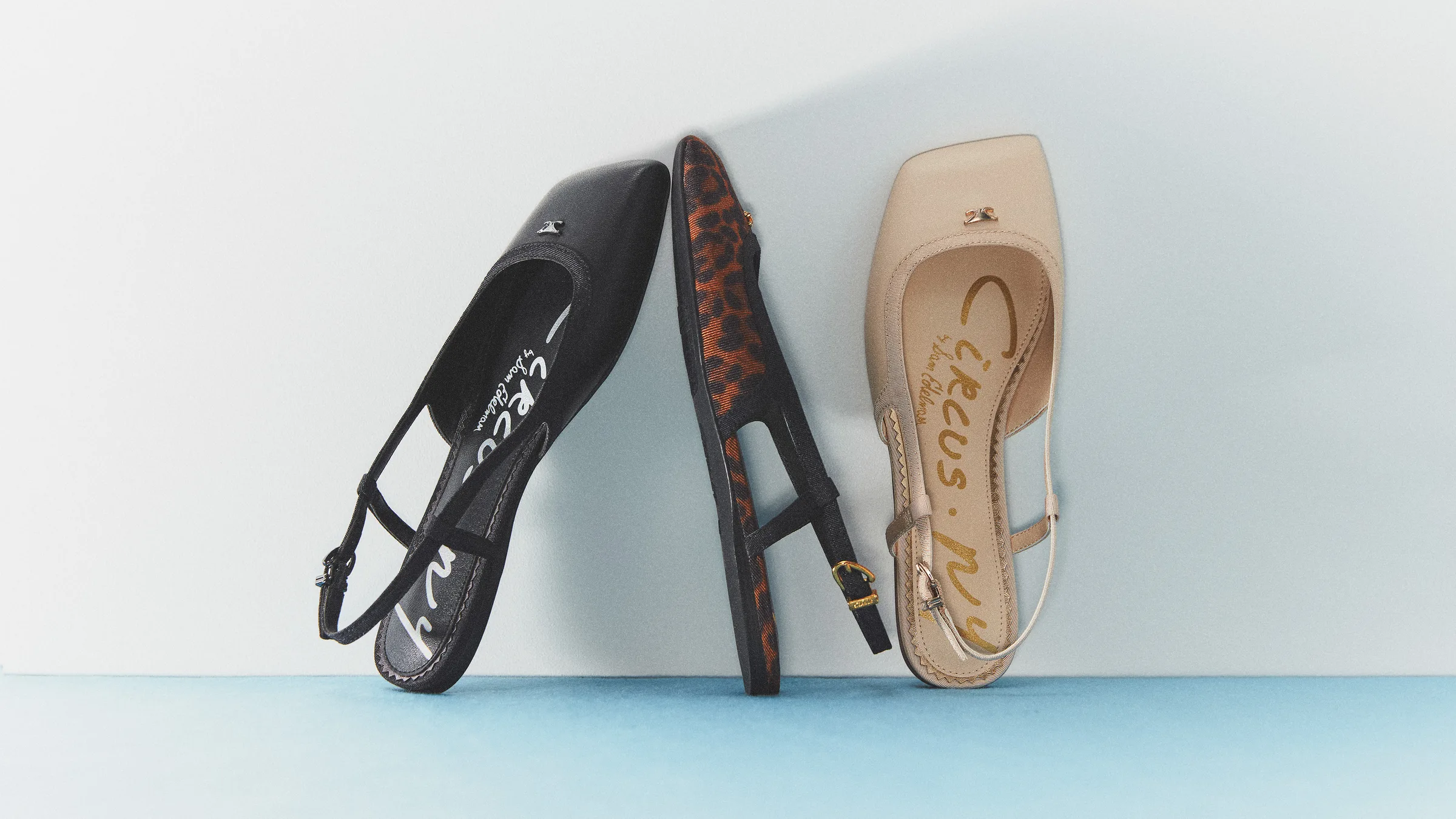 Three slingback flats in black, leopard and vanilla leather leaning on a white wall over a blue floor, for Circus NY.