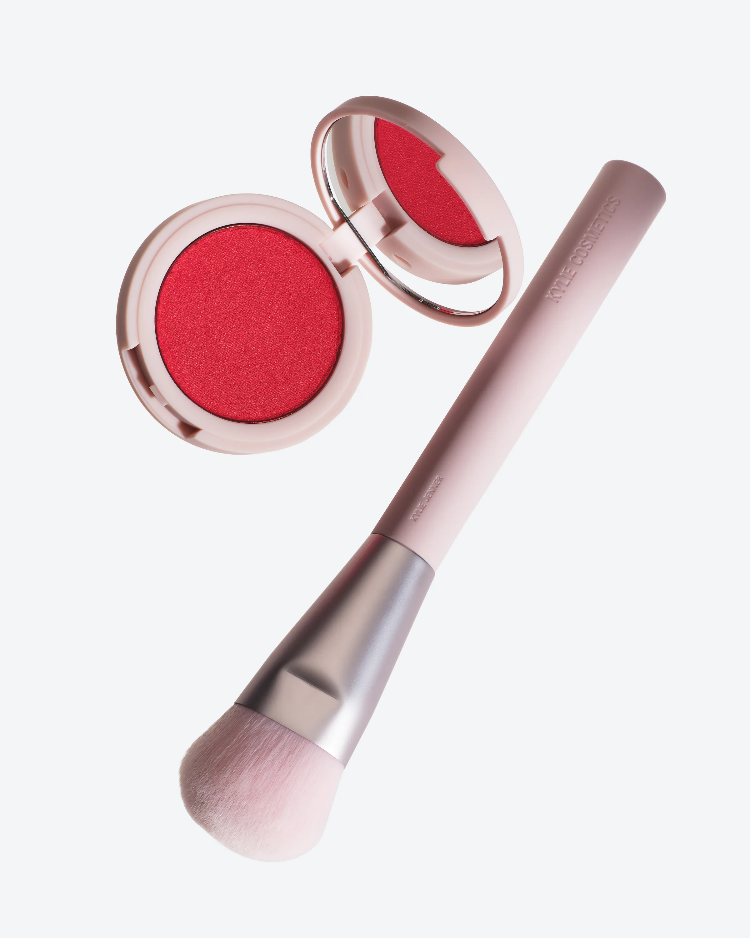 Open pink compact of red Lady Bug hybrid blush beside a pink blush brush on a pale grey background, for Kylie Cosmetics.