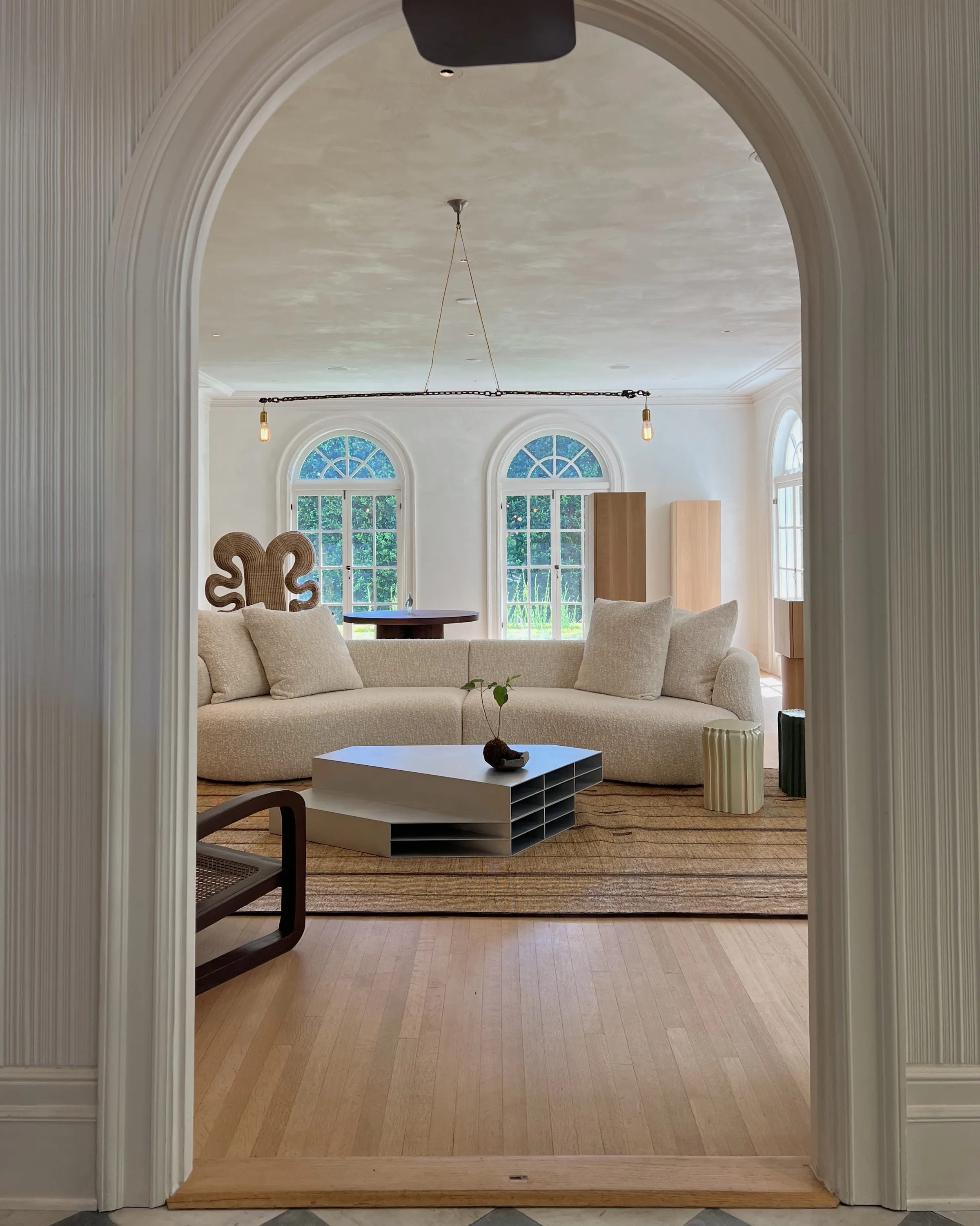 Bright living room seen through an arched doorway, with a curved boucle sofa, low coffee table and arched windows, for Jennifer Hagler.