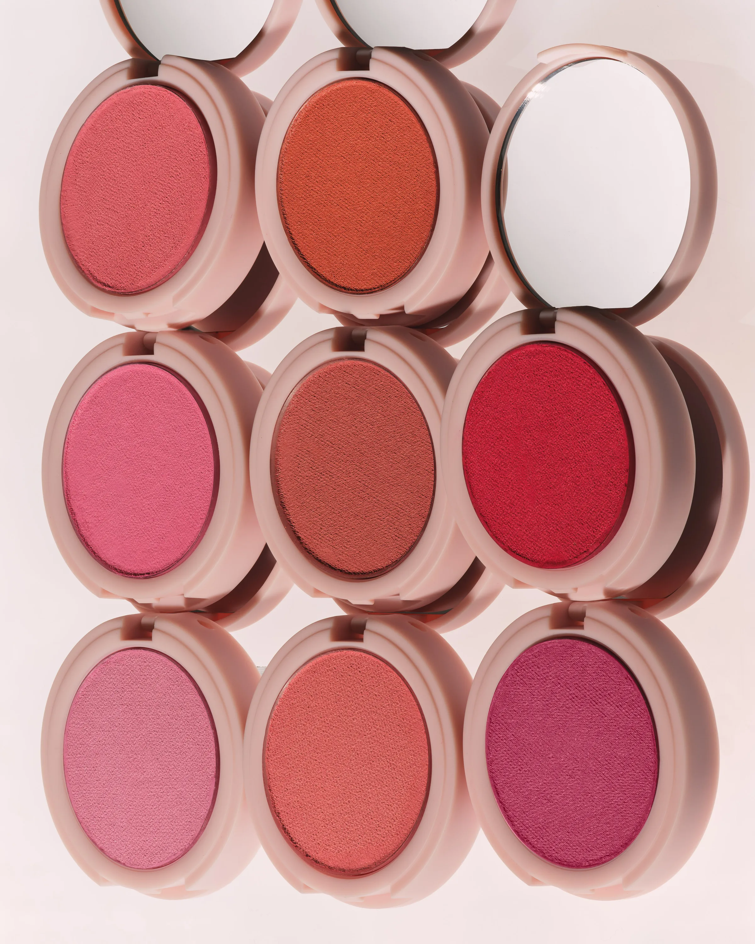 Nine open pink blush compacts in shades from coral to berry arranged in a grid with mirrored lids, for Kylie Cosmetics.