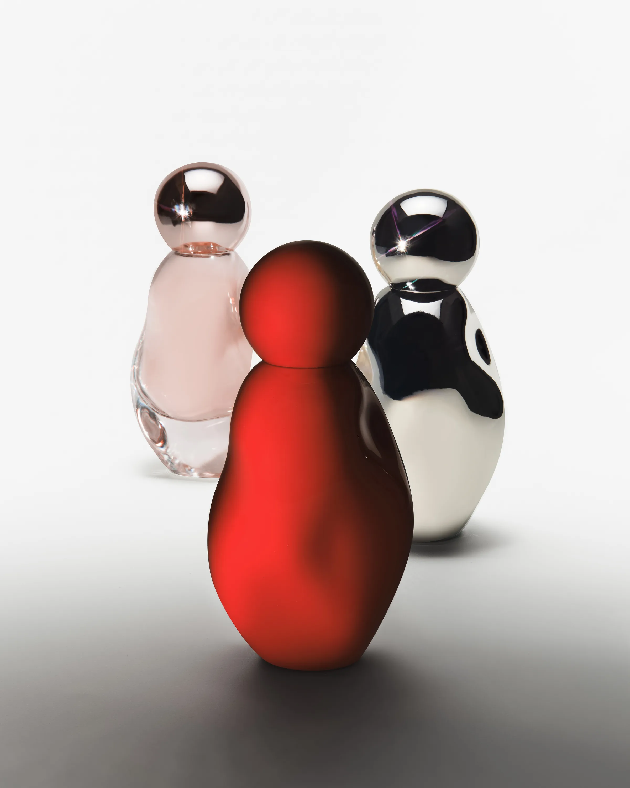 Three Cosmic perfume bottles in red, clear pink and chrome on a white-to-grey gradient, still life, for Kylie Cosmetics.