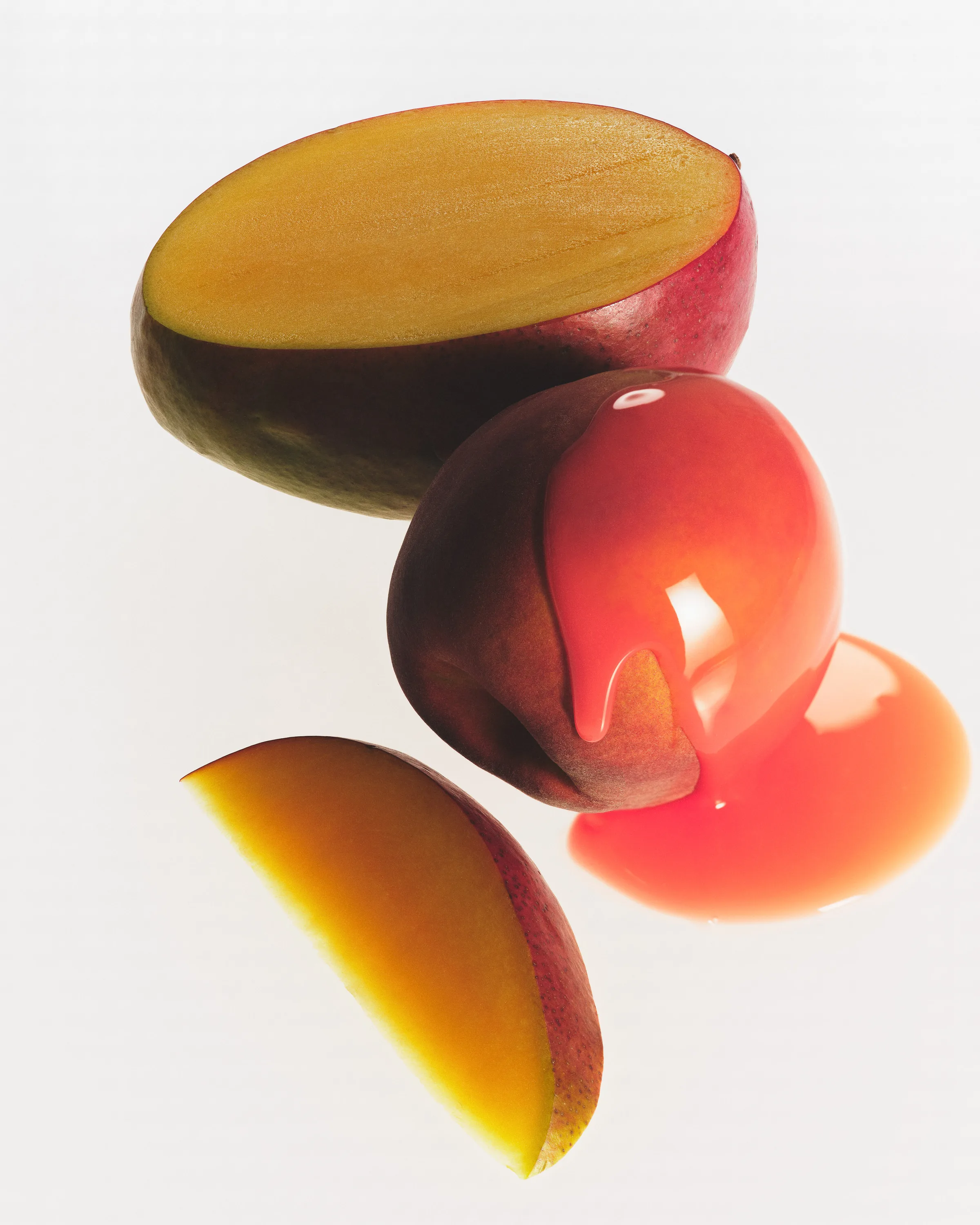 Halved mango and slice beside a whole mango coated in glossy pink-orange liquid on white, for Kylie Cosmetics.