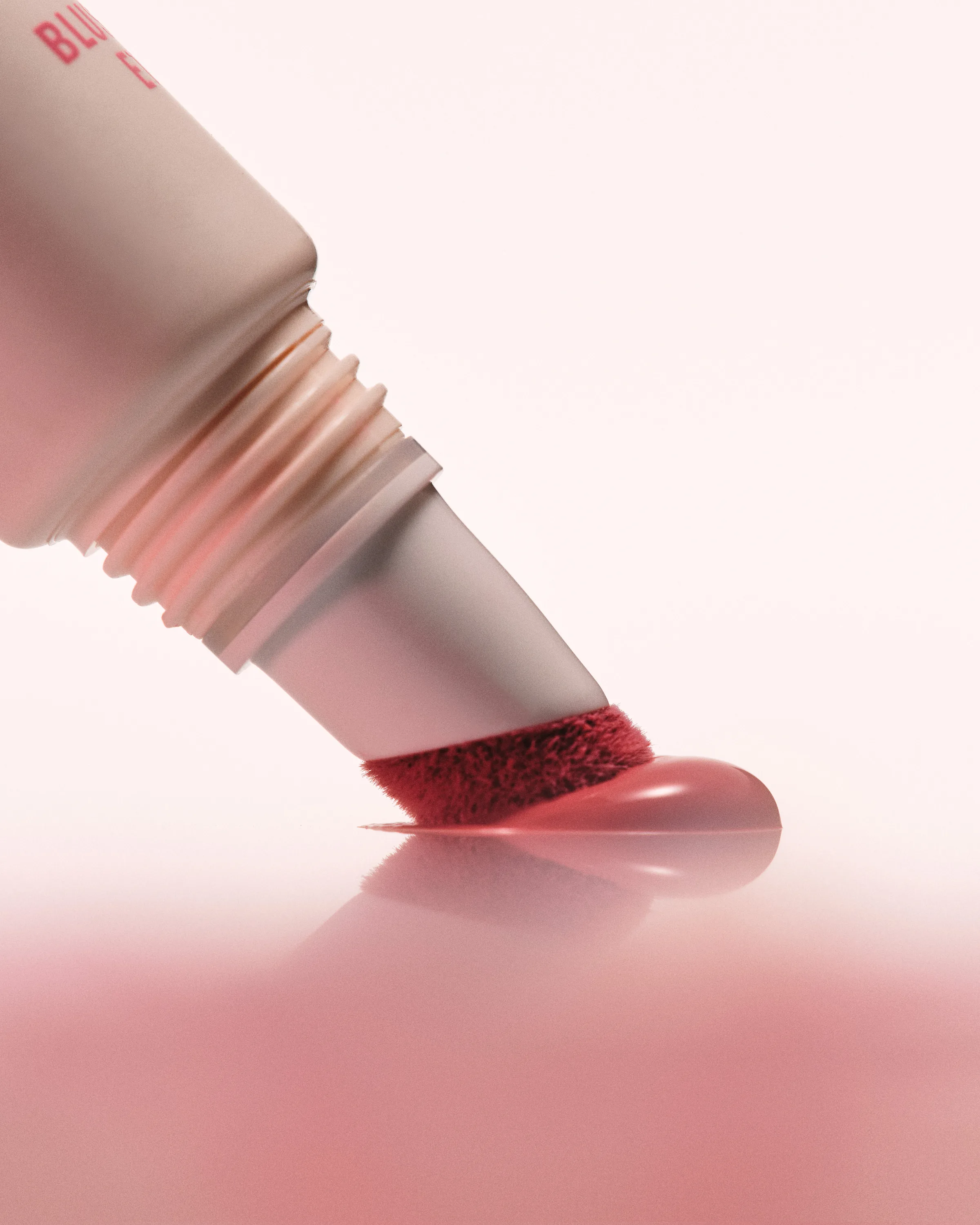 Liquid blush tube with a red sponge-tip applicator pressing a pink dot onto a glossy pink surface, for Kylie Cosmetics.