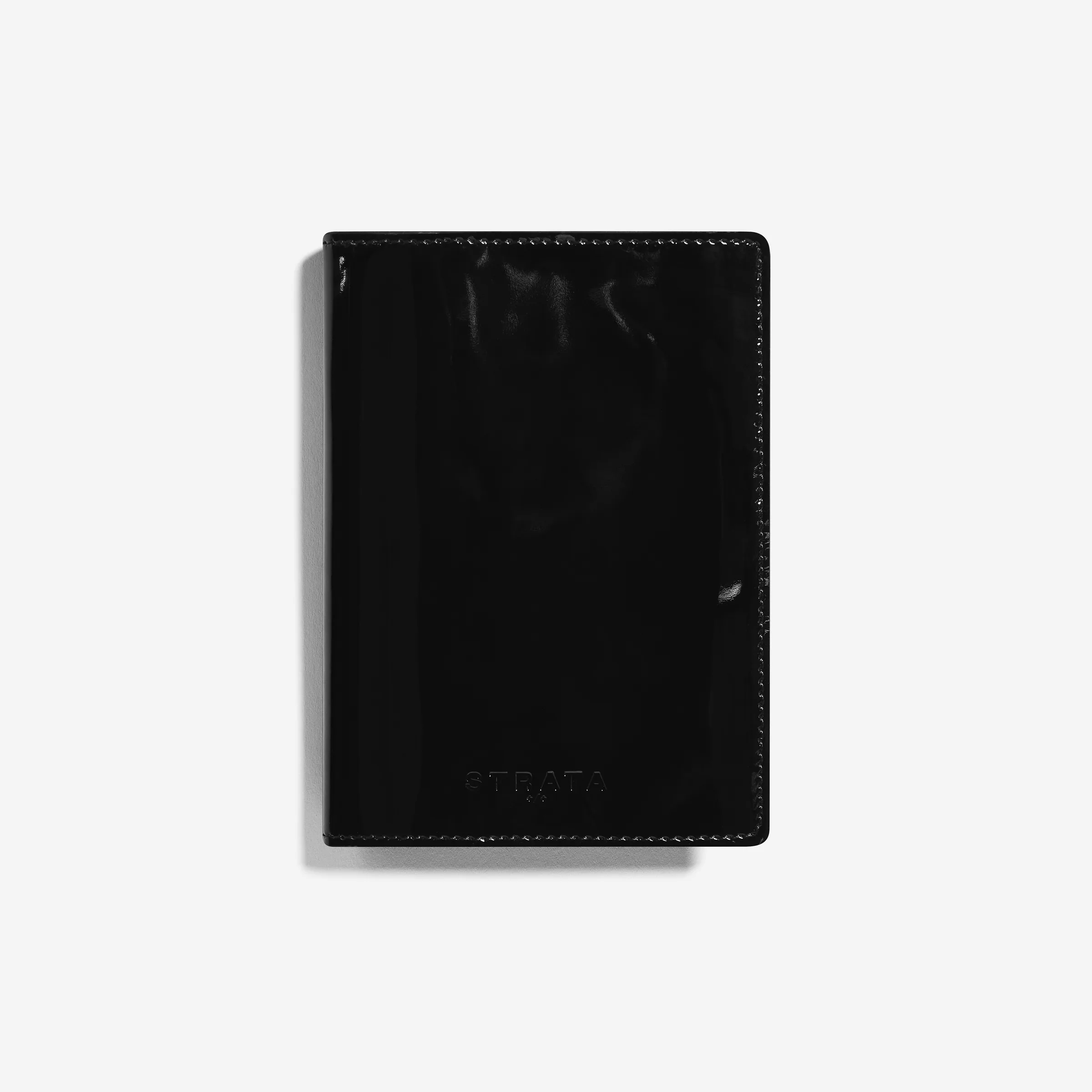 Black patent leather travel sleeve with embossed logo, shot flat on a white background, for Strata.