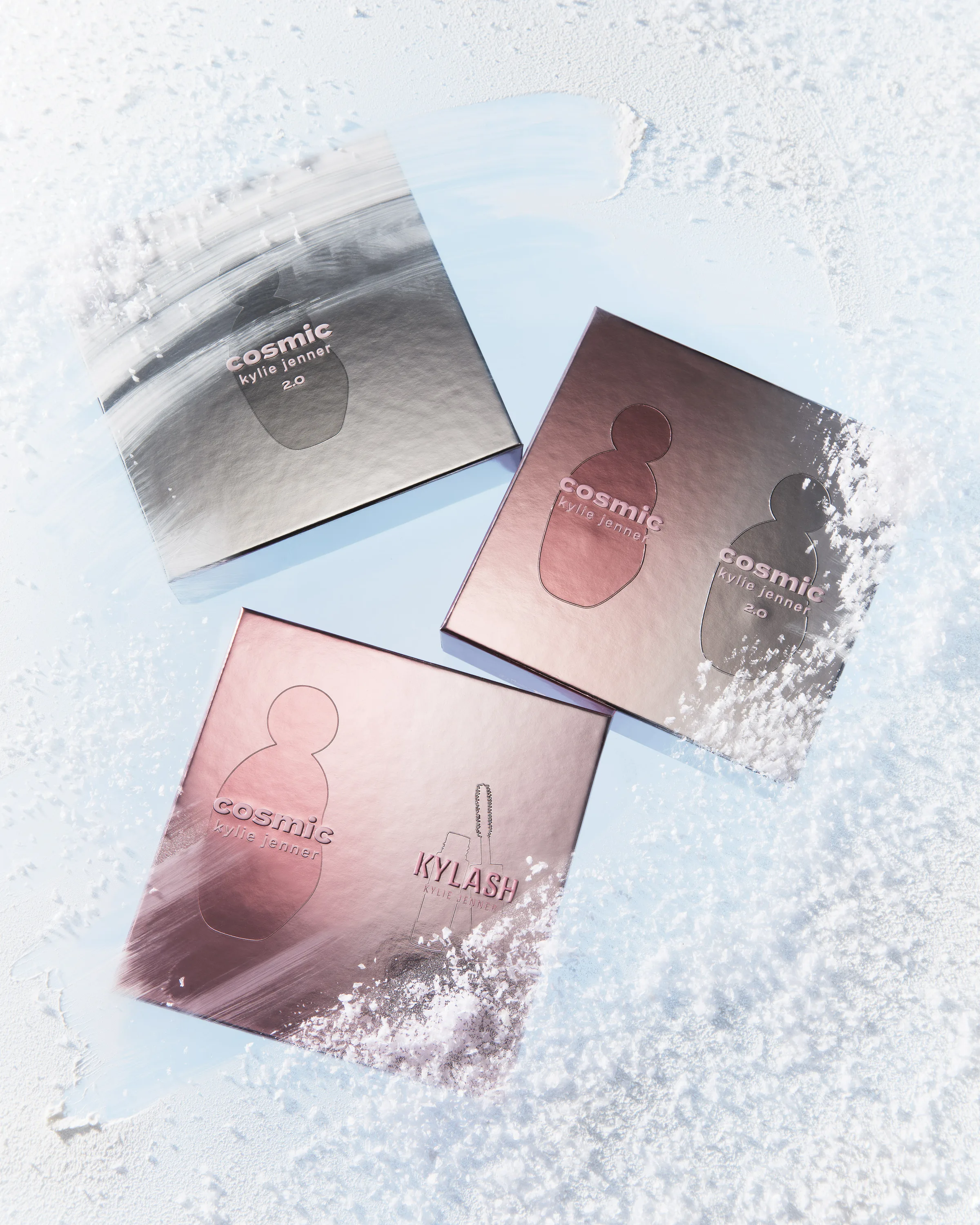 Three metallic Cosmic Kylie Jenner gift boxes in silver and pink lying in powdery snow, for Kylie Cosmetics.