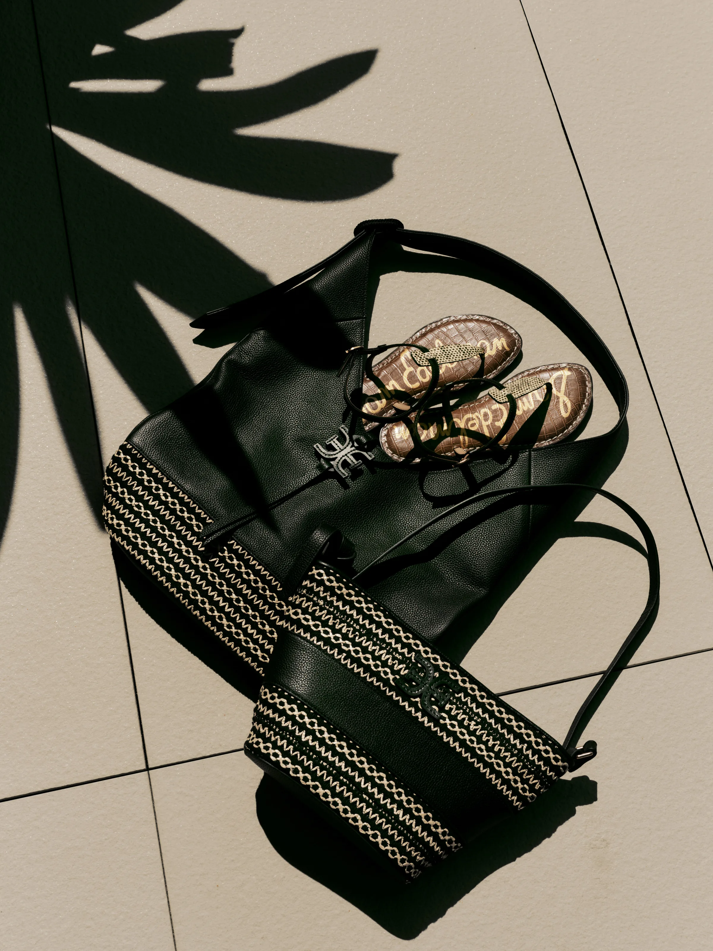 Black leather totes with woven stripes and black thong sandals on sunlit tiles under palm shadows, for Sam Edelman.