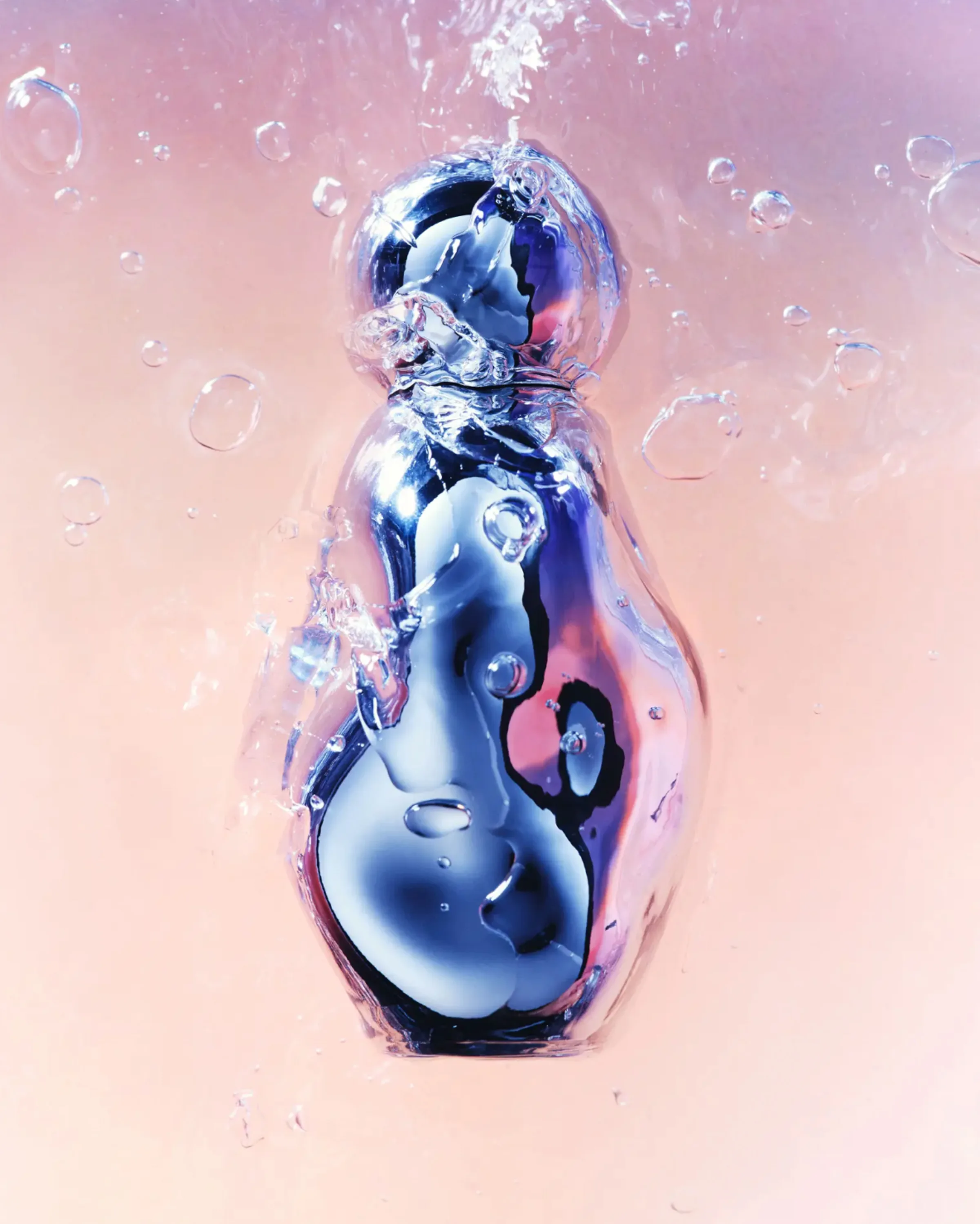 Chrome perfume bottle plunging into water with bubbles against a soft pink background, for Kylie Cosmetics.