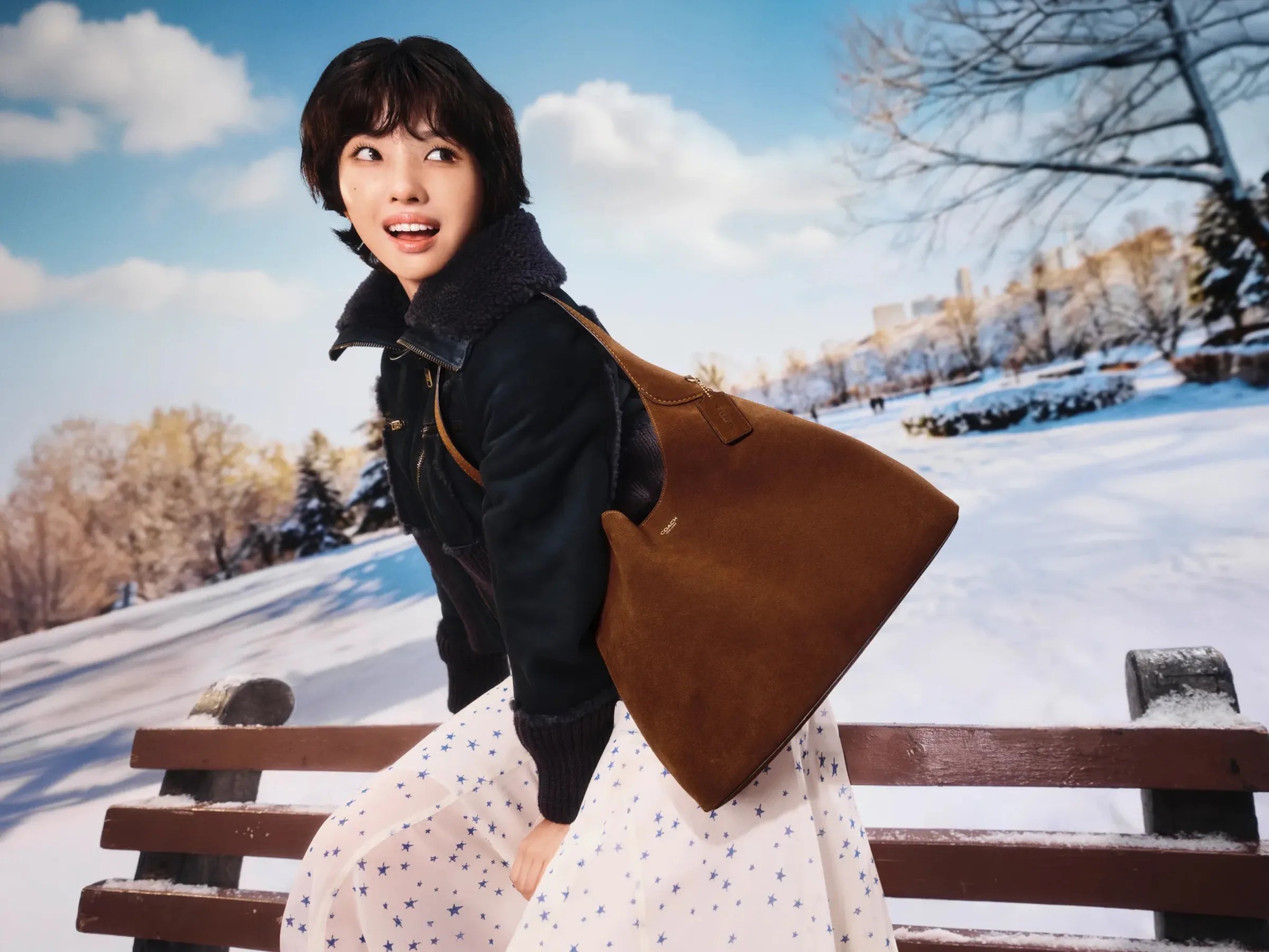 AI image of a woman with a brown suede shoulder bag and shearling jacket by a snowy park bench, for Coach.
