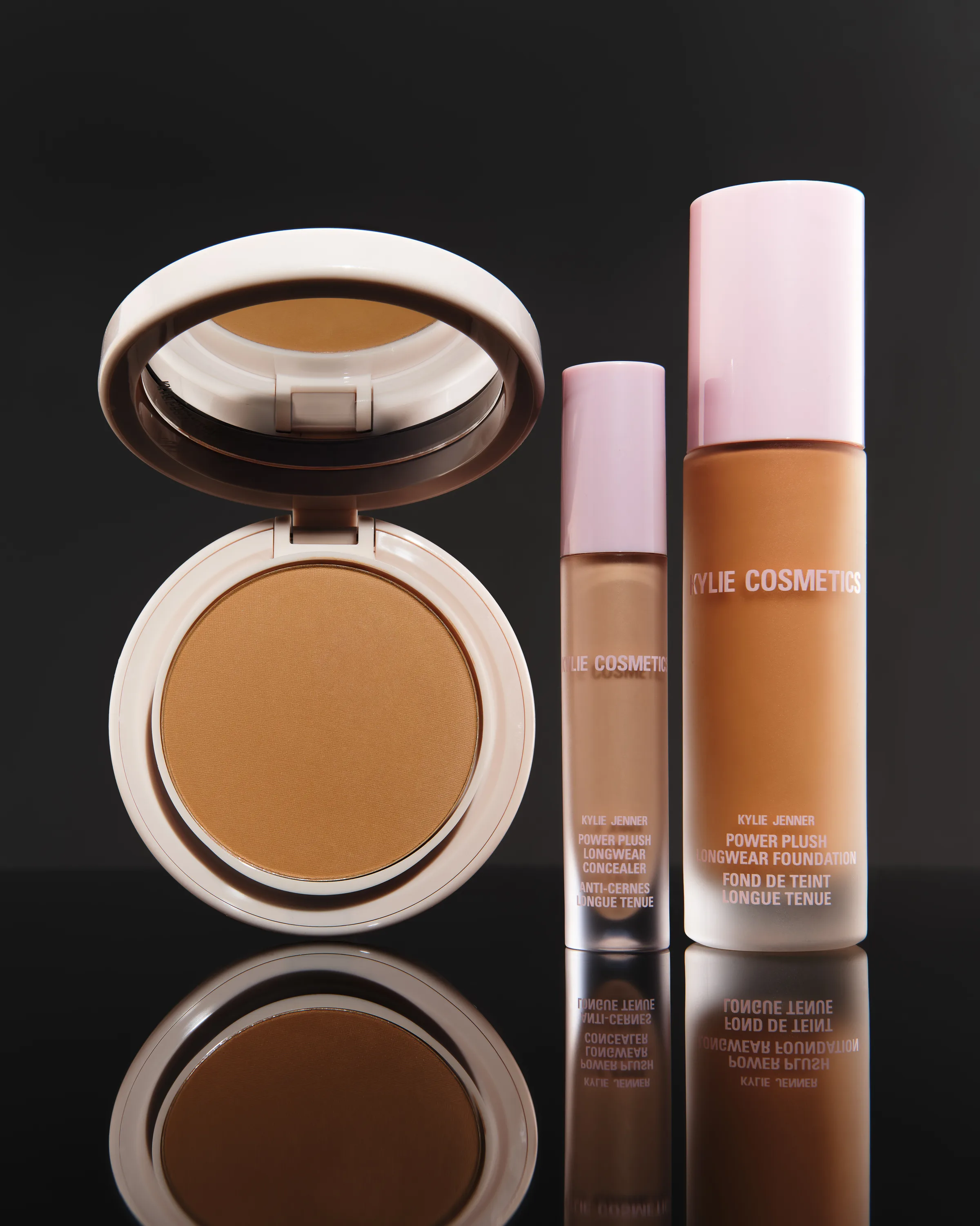 Open powder compact, concealer and Power Plush foundation in a tan shade on glossy black with reflections, for Kylie Cosmetics.