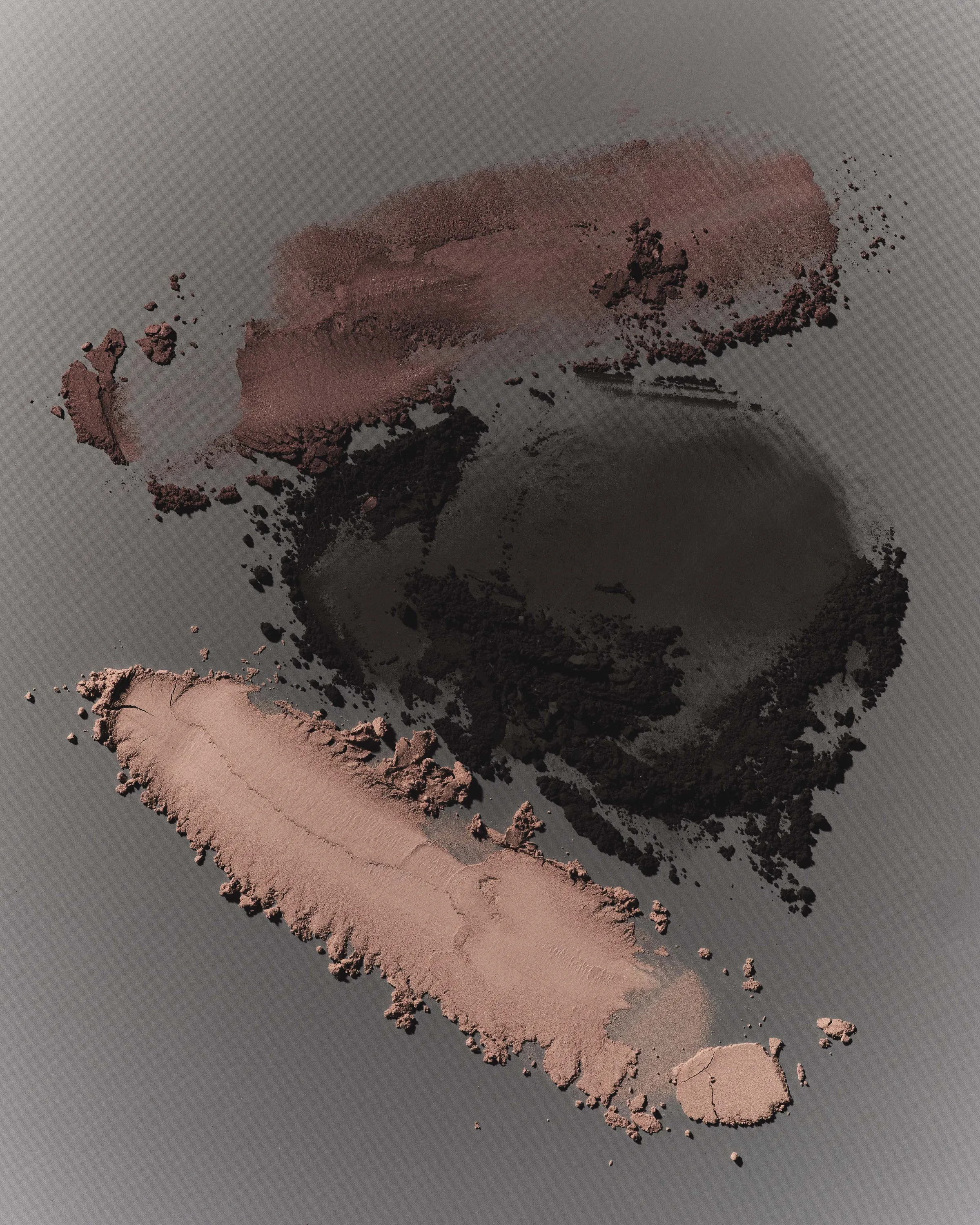 Crushed eyeshadow swatches in mauve, charcoal and nude smeared across a grey ash background, for Kylie Cosmetics.