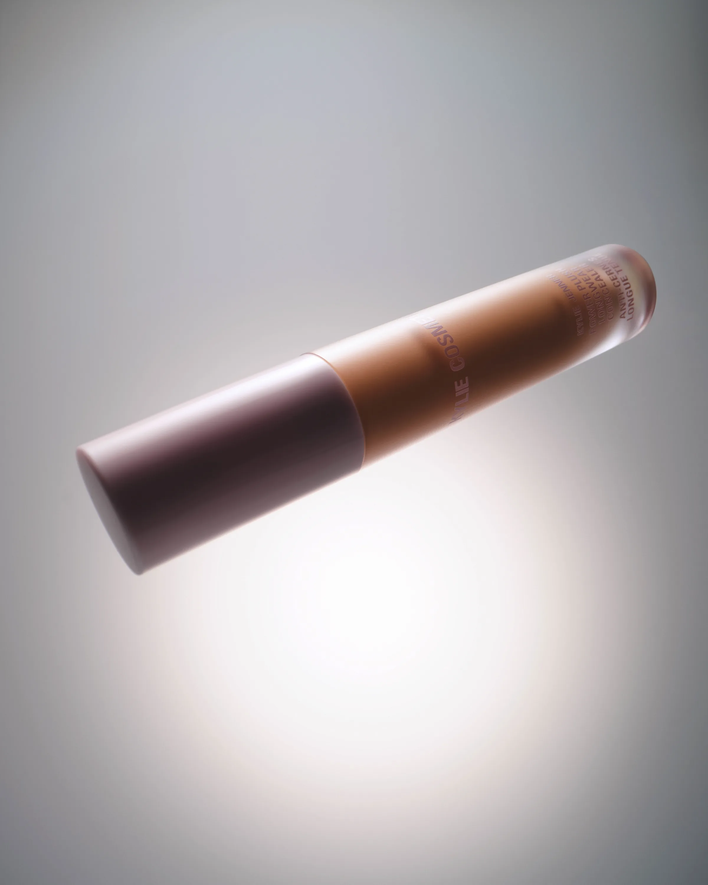 Concealer tube with mauve cap floating at an angle against a glowing grey backdrop, for Kylie Cosmetics.