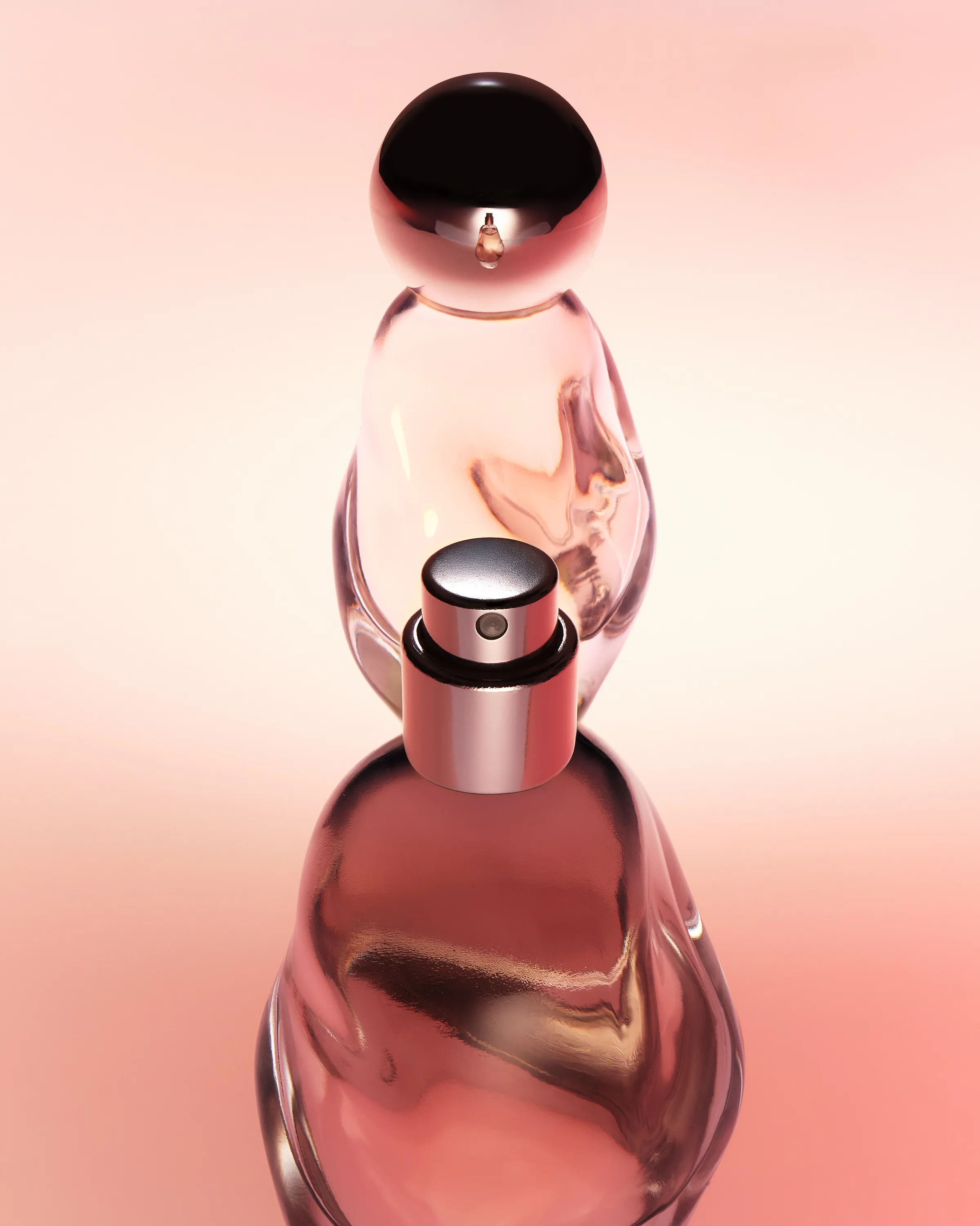 Two pink glass perfume bottles with chrome caps stacked on a glossy surface against a soft peach backdrop, for Kylie Cosmetics.