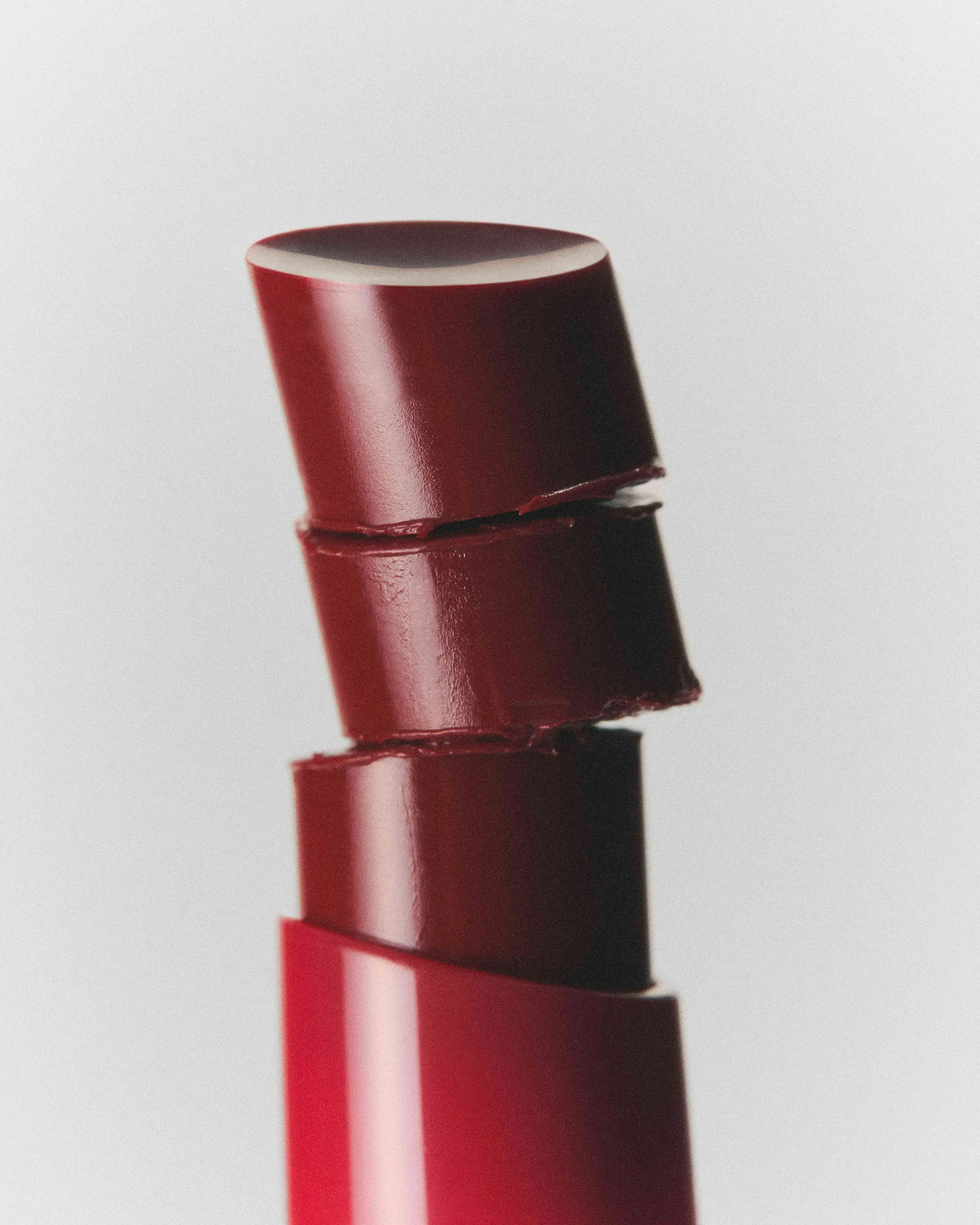 Still life of a deep red lipstick bullet cut into stacked, offset slices on a pale grey backdrop, for Kylie Cosmetics.