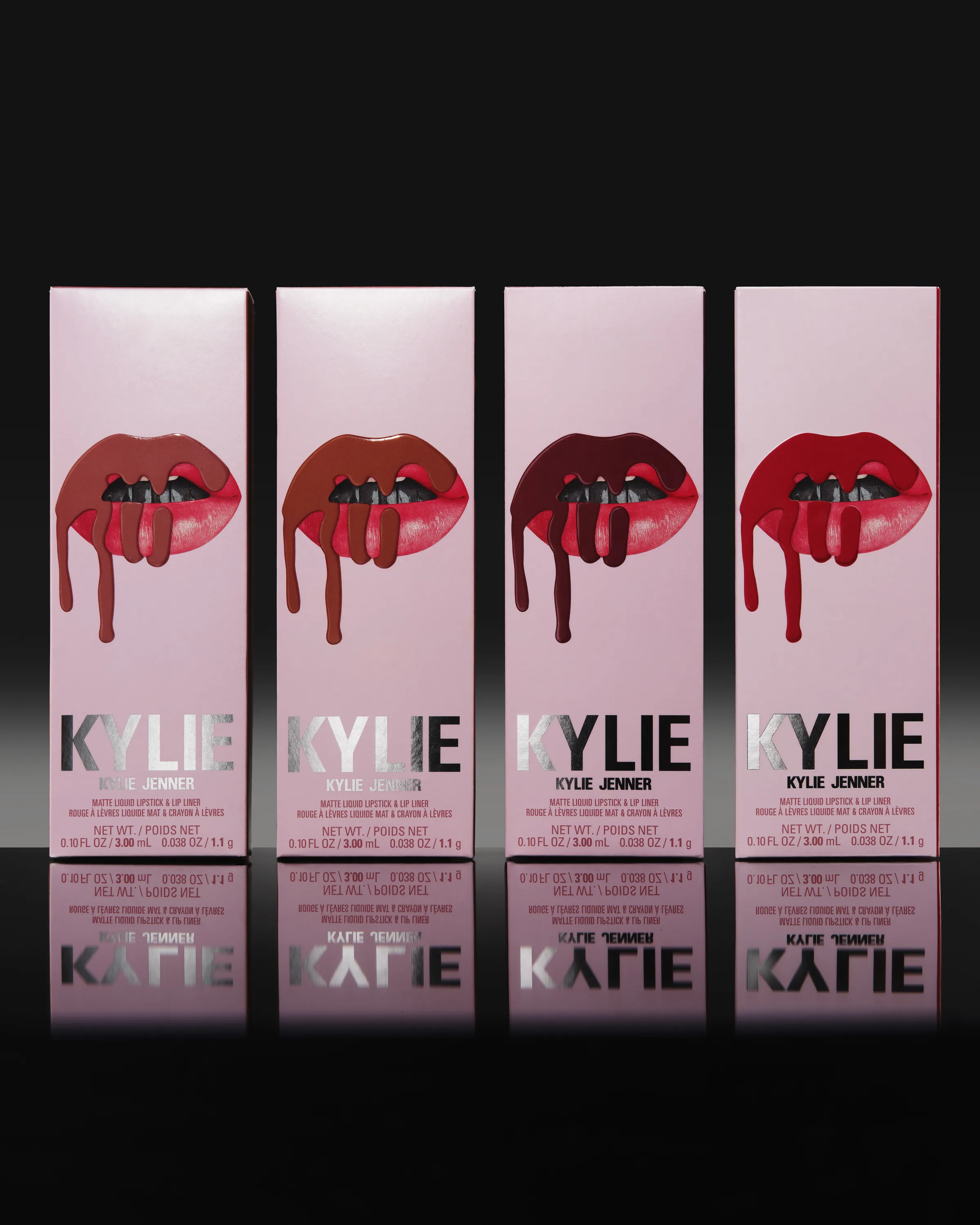 Four pink lip kit boxes with dripping lip graphics in nude to red shades, reflected on a glossy black surface, for Kylie Cosmetics.