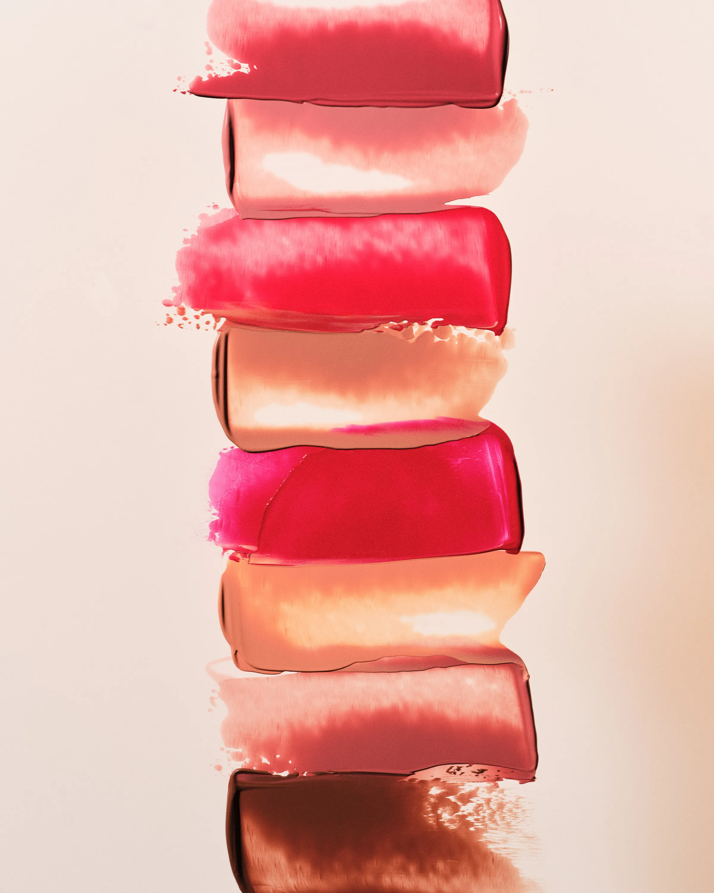 Vertical stack of lipstick swatches in pinks, nudes and browns smeared on a cream background, for Kylie Cosmetics.