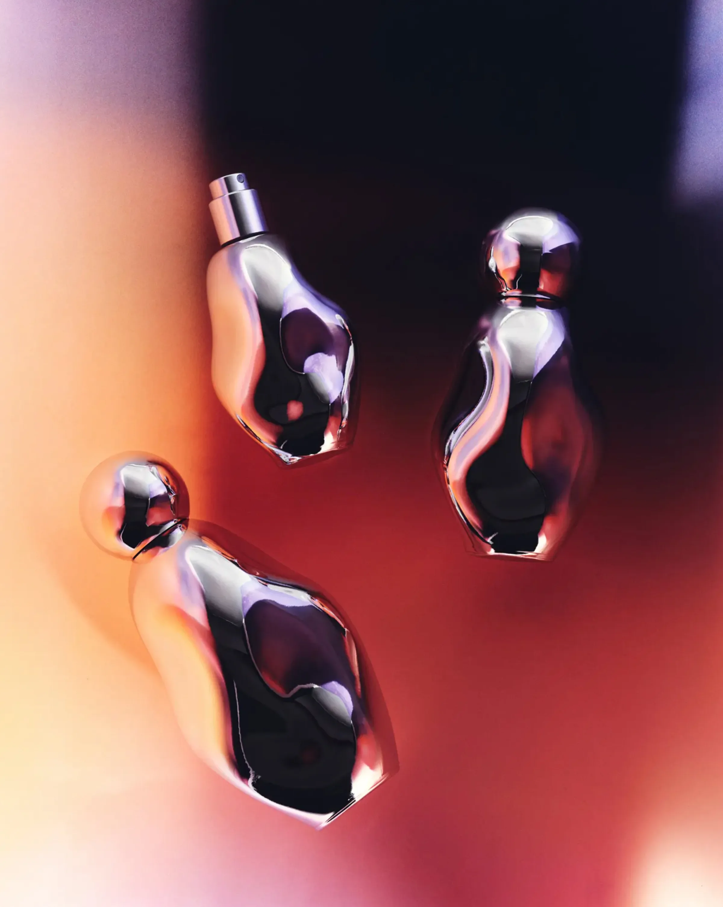 Three sculpted chrome perfume bottles floating against a blurred orange and purple backdrop, for Kylie Cosmetics.